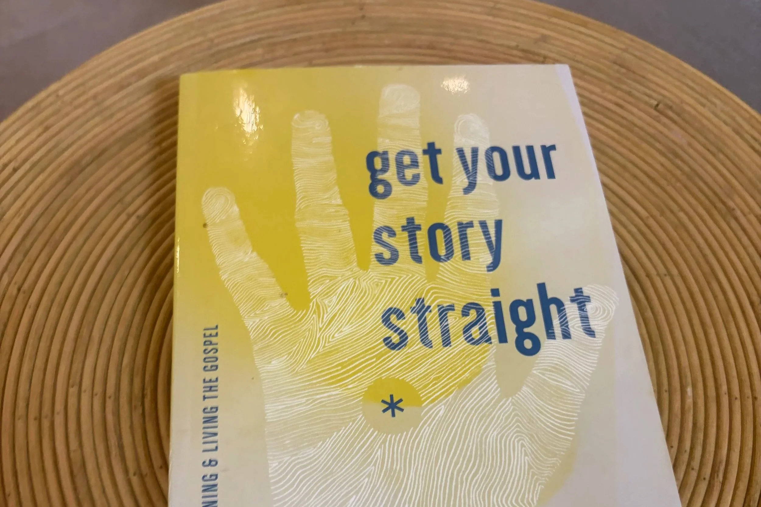 A yellow book with blue text and fingerprint graphics placed on a round wooden table. The visible part of the text says 'get your story straight'.