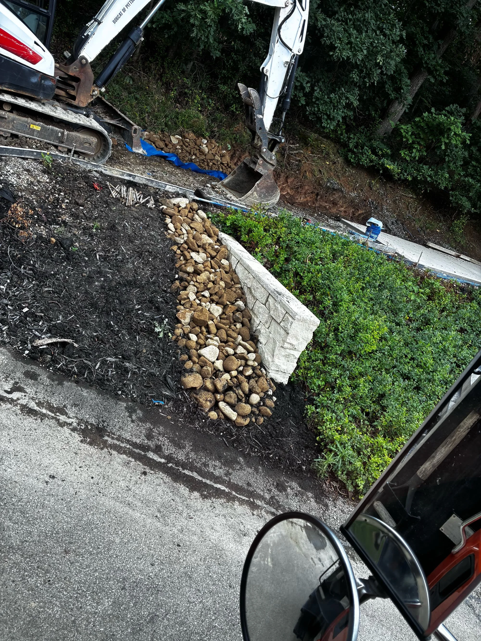 Mini excavator grading a site beside a new stone retaining wall in Butler, PA