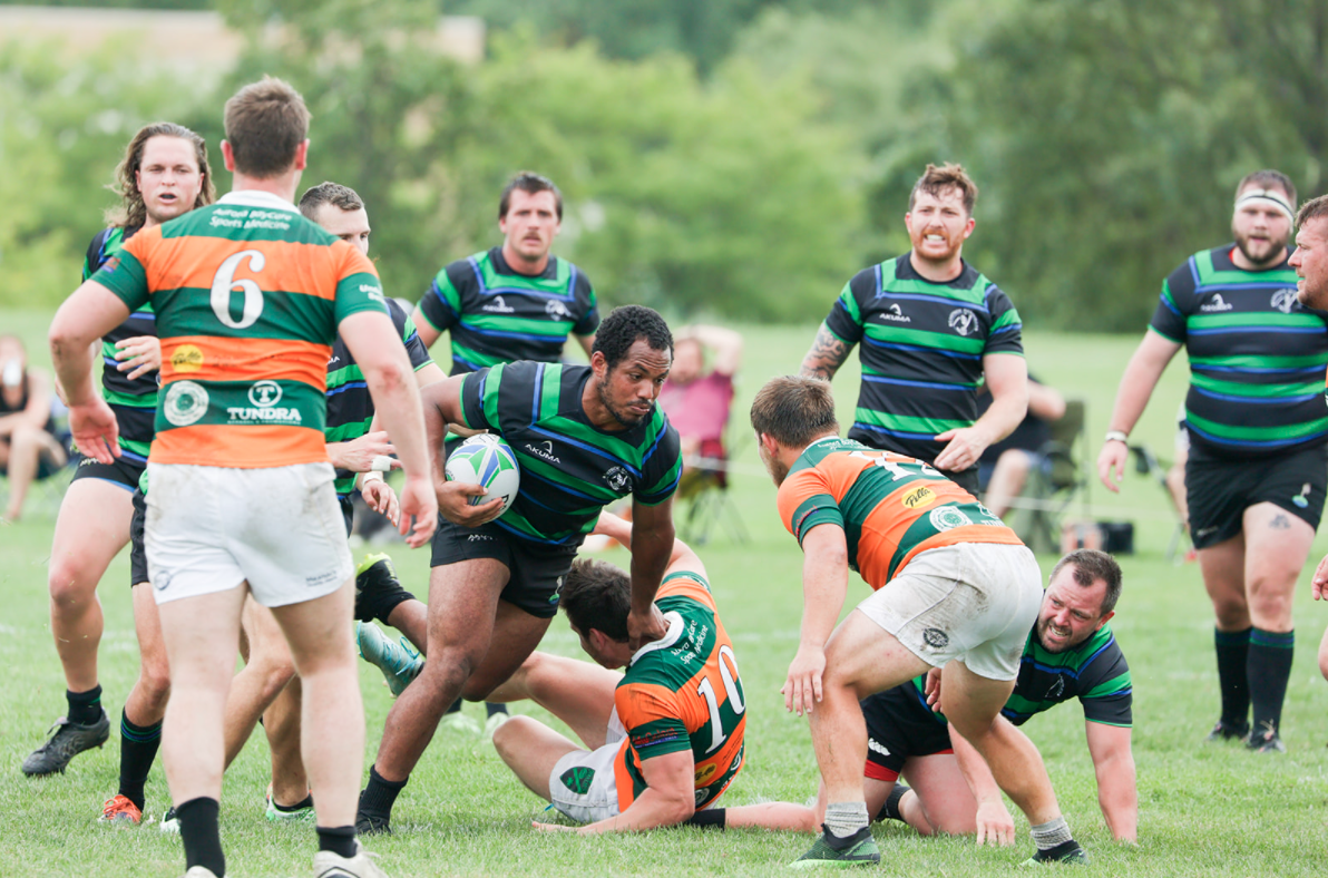 Rugby players in green and orange jerseys competing for the ball on a grassy field during a match.