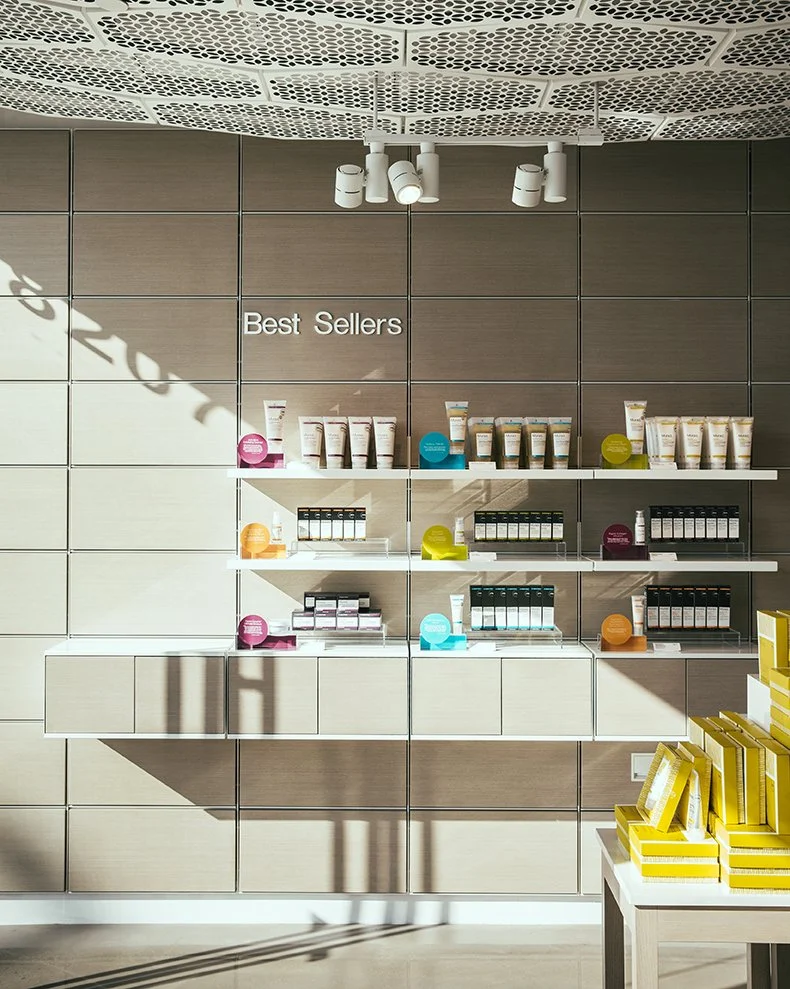 Retail display shelf labeled 'Best Sellers' with skincare or cosmetic products arranged on white shelves and colorful circular signs, set against a wooden-paneled wall.