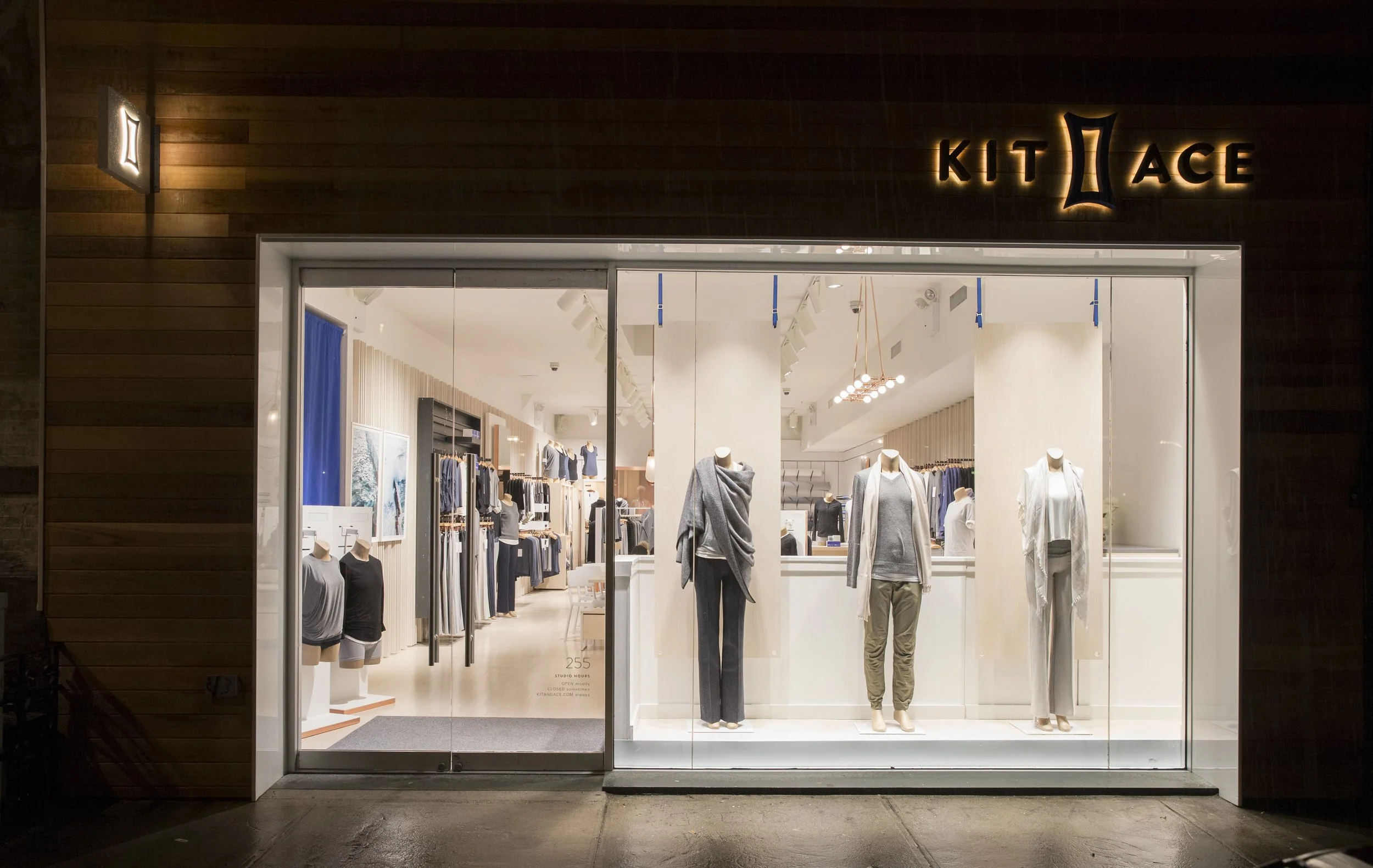 Clothing store front with mannequins displaying casual clothing inside, illuminated sign reads 'KIT LACE'.