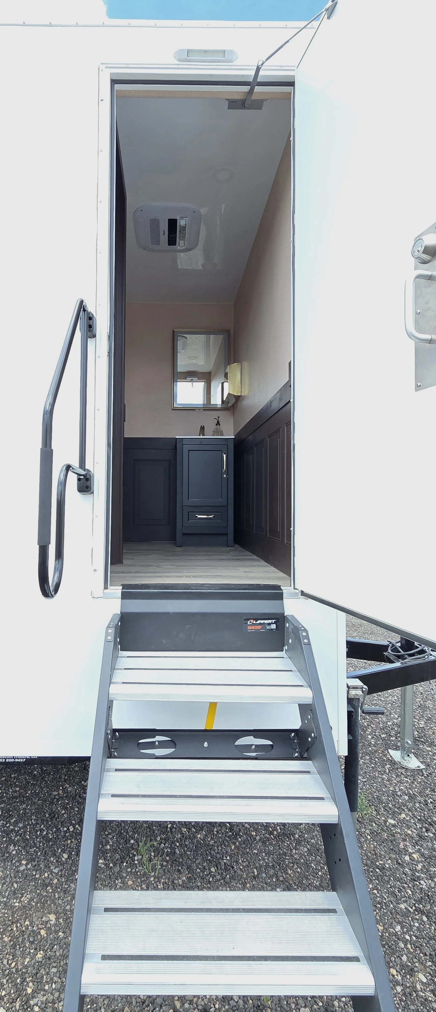 Inside view of a portable FIESTA LUXURY RENTAL trailer bathroom with a black vanity, mirror, sink, and light-colored walls.