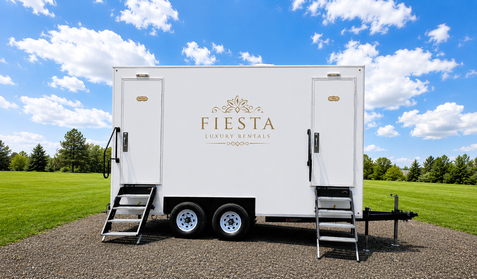 White mobile Fiesta luxury rental trailer with "Fiesta Luxury Rentals" logo, black stairs, and black handles, set against a green field and blue sky with clouds.