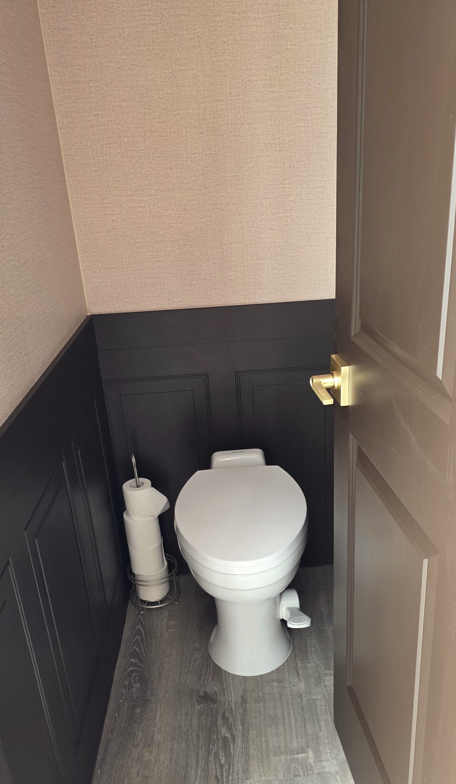 FIESTA LUXURY RENTAL BATHROOM are Spacious bathroom with a white toilet, brown wainscoting walls, and beige textured wallpaper, with a toilet paper roll on a stand.