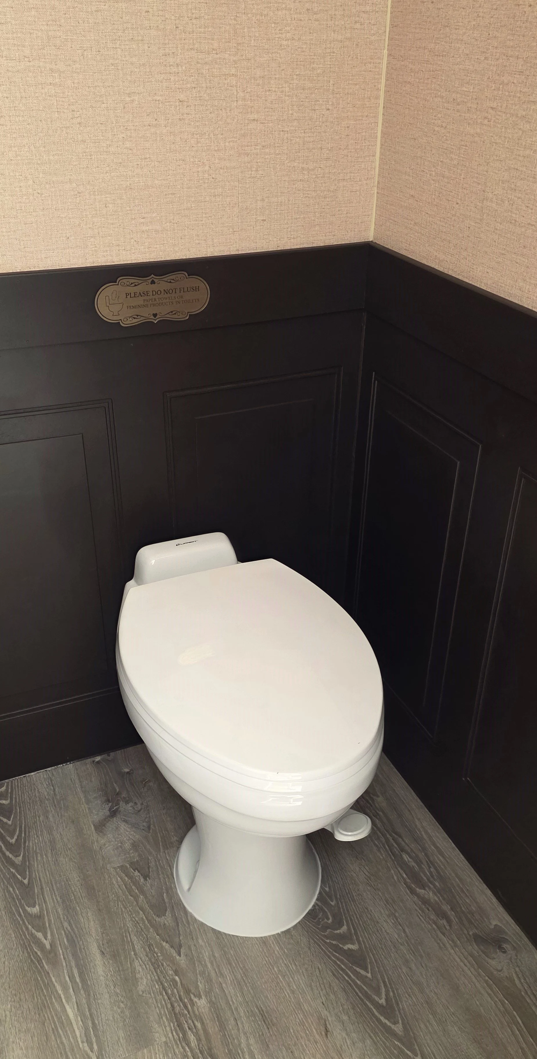 A FIESTA LUXURY RENTAL RESTROOM with white toilet in a restroom with dark wood paneling on the walls and a sign that says 'Please do not flush paper towels or feminine products in toilets'.