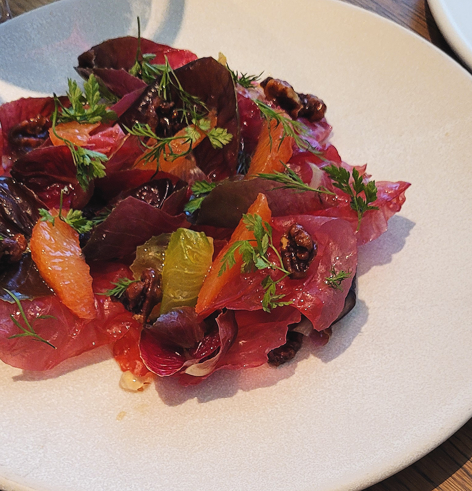 A plate of beetroot salad, blood orange slices, pecan, and garnishes of herbs on a white plate.