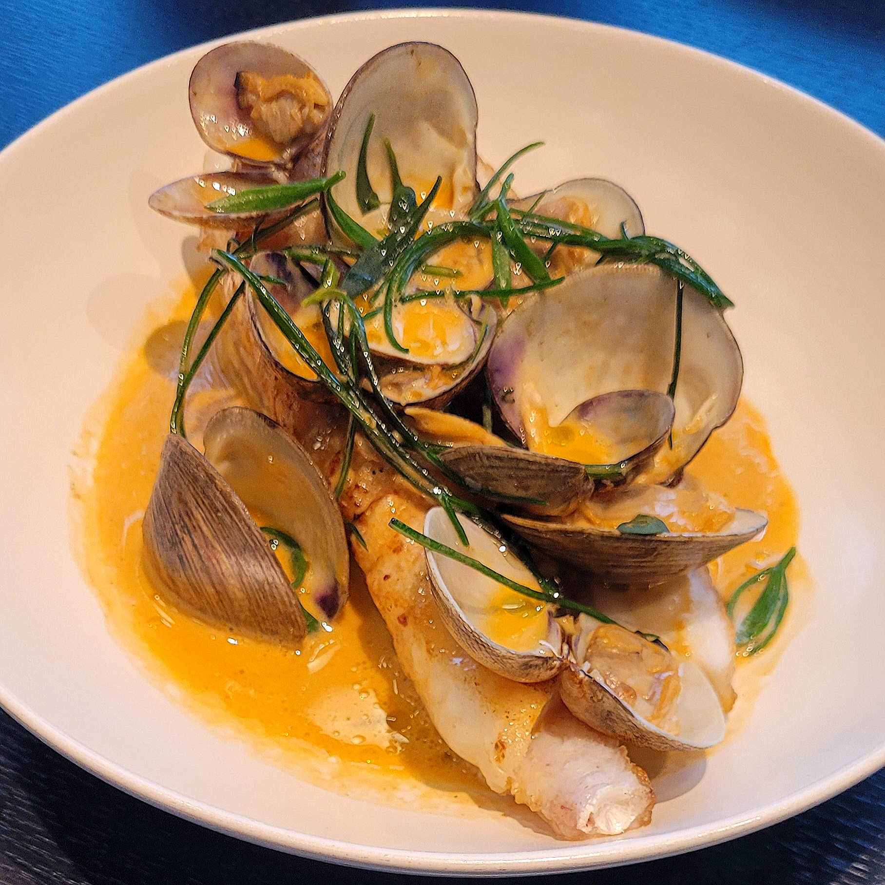 Barbequed monkfish and Cclams with samphire on a white plate with a shellfish sauce.