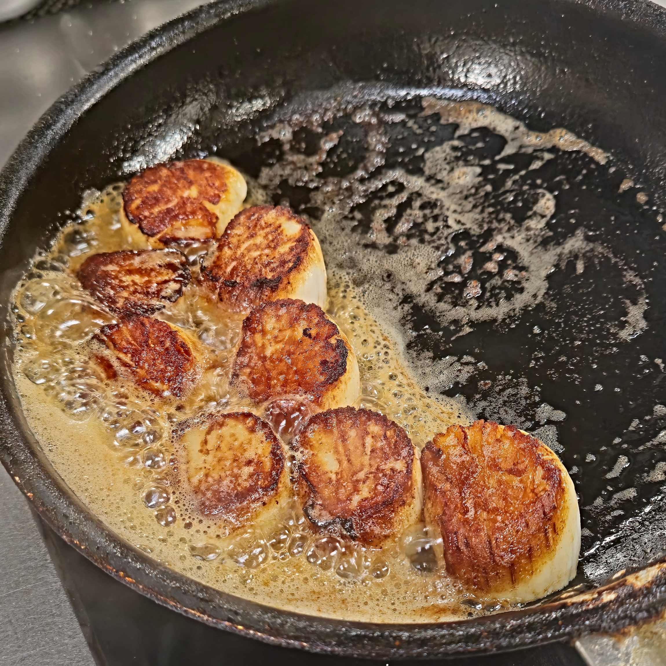 Close-up of scallops being seared in a black skillet with bubbling butter.