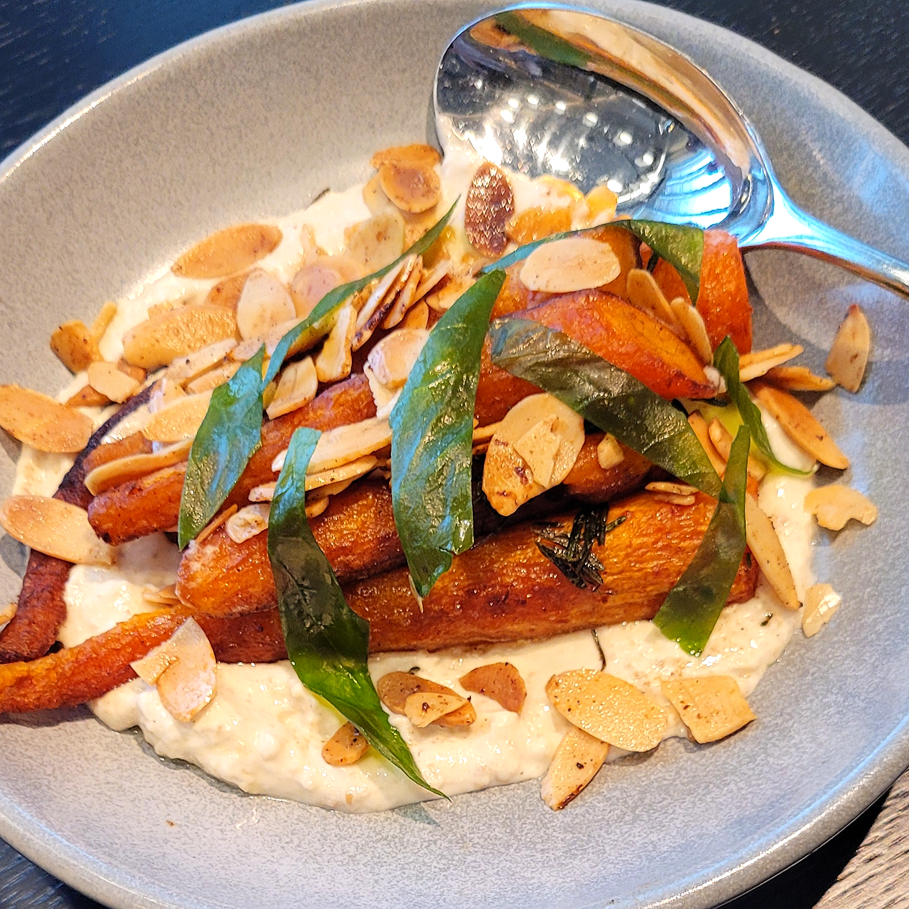 Close-up of a dish with grilled fish, topped with sliced almonds, fresh herbs, and a creamy sauce, served on a ceramic plate.
