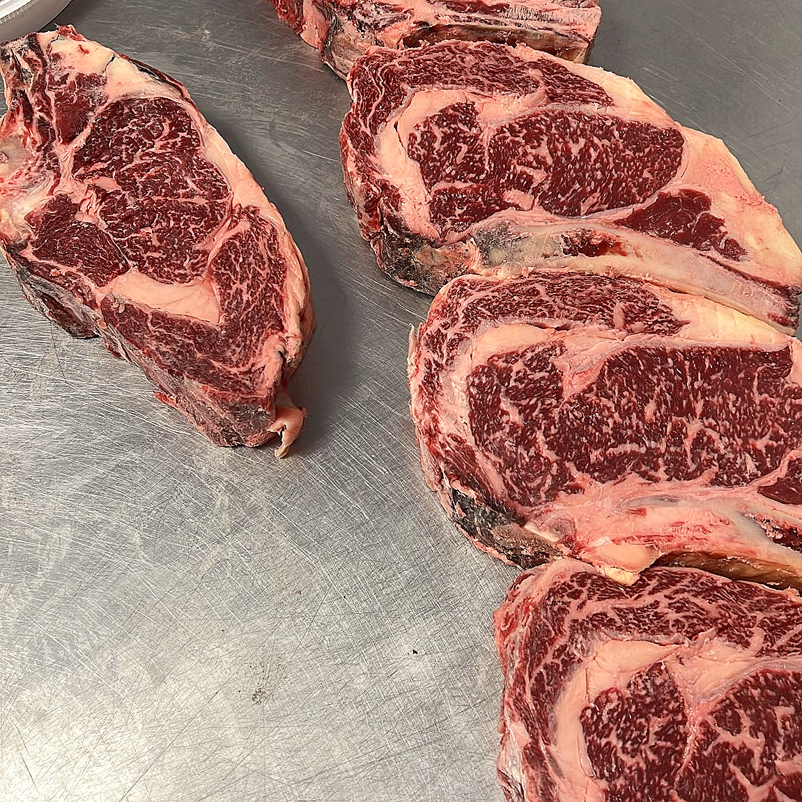 Several raw USDA Prime beef steaks with marbled fat on a metal surface.
