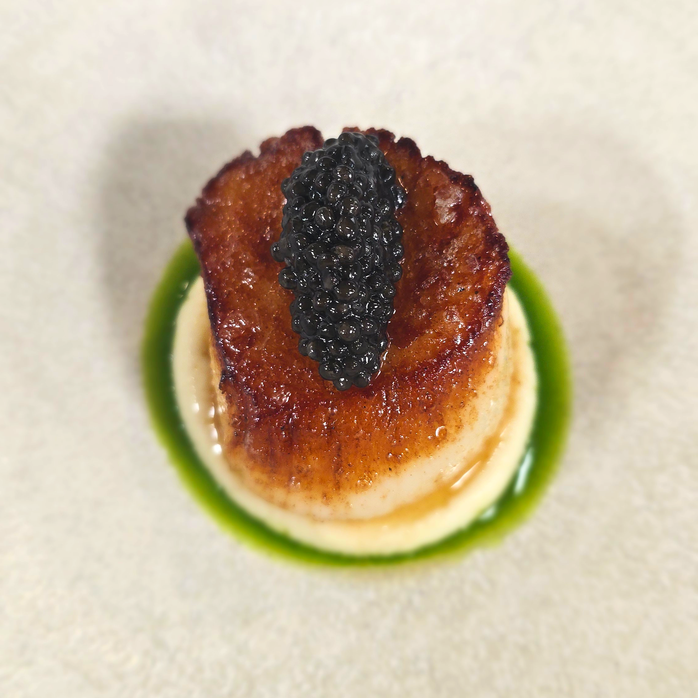 Close-up of a seared scallop topped with black caviar.