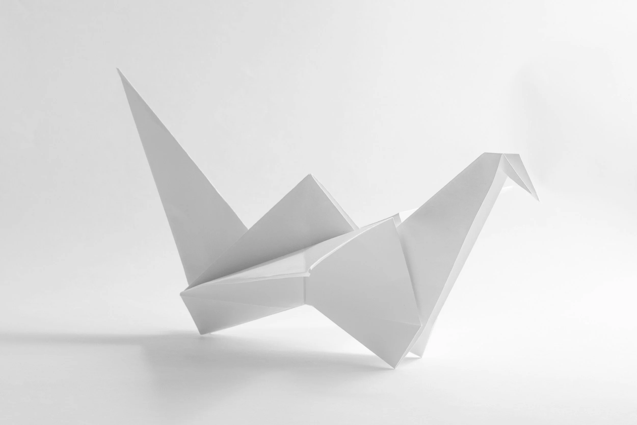 A white paper origami crane with sharp, angular folds, set against a plain white background.
