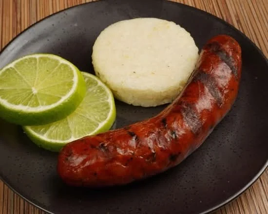 Cooked sausage, mashed potato, and lime slices on a black plate.