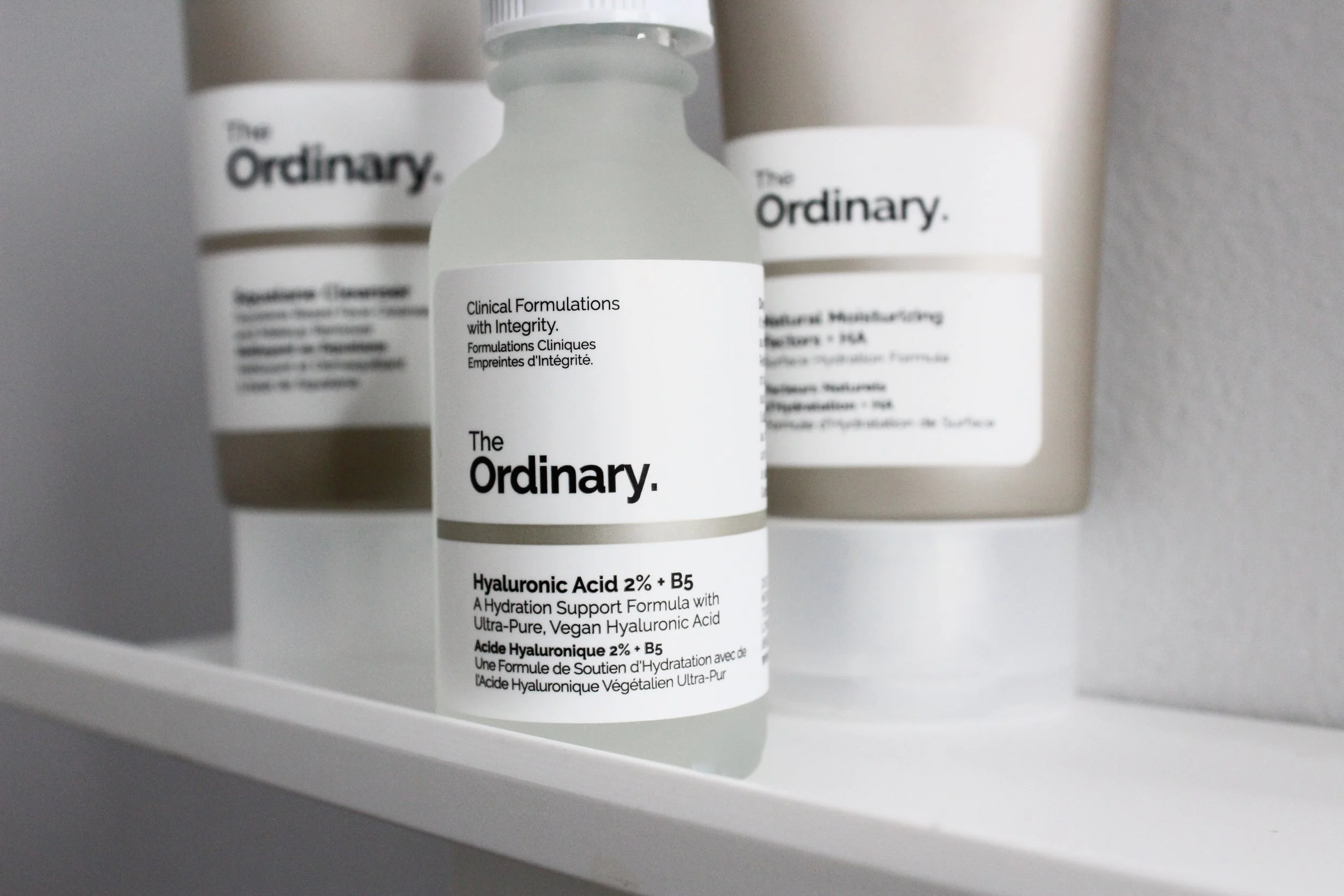 Close-up of three skincare bottles from The Ordinary, with the middle one showing labels for a hyaluronic acid serum.