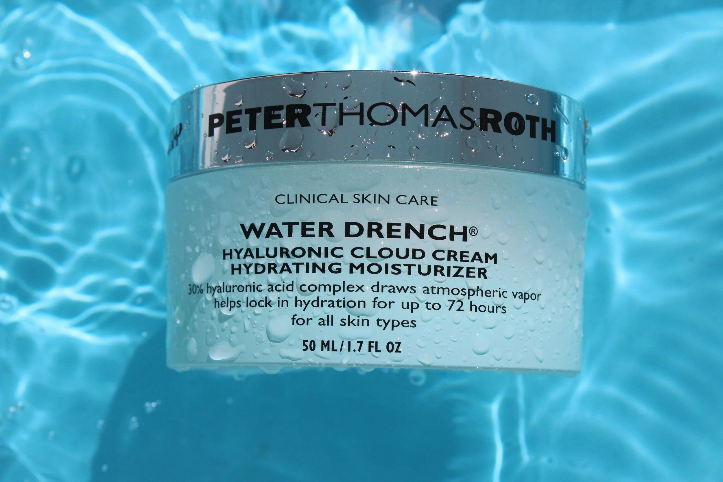 Close-up of skincare product container labeled 'Water Drench' by Peter Thomas Roth, surrounded by water with droplets, emphasizing hydration.