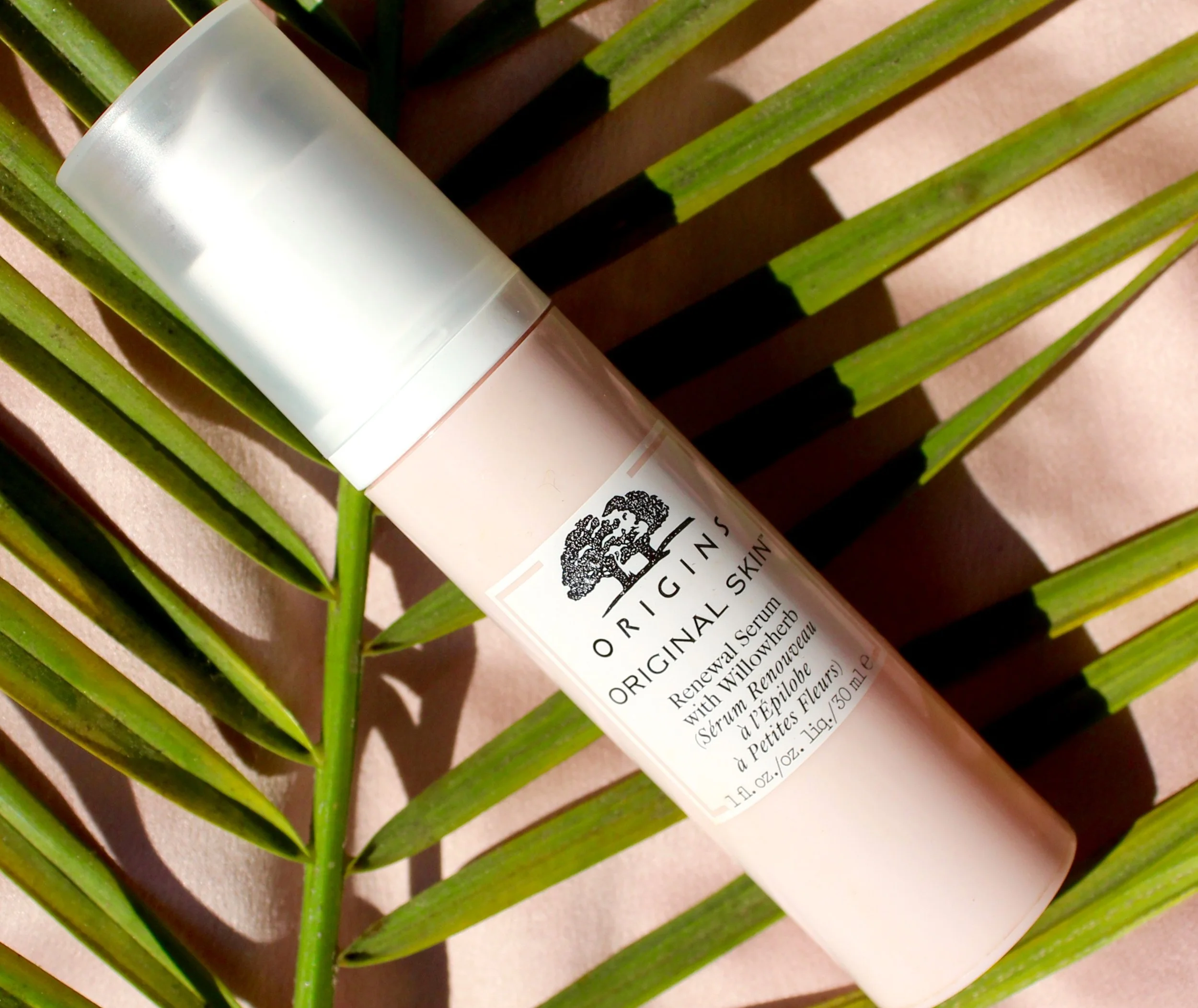 A skincare product bottle resting on a wooden slatted surface with green palm leaves casting shadows.