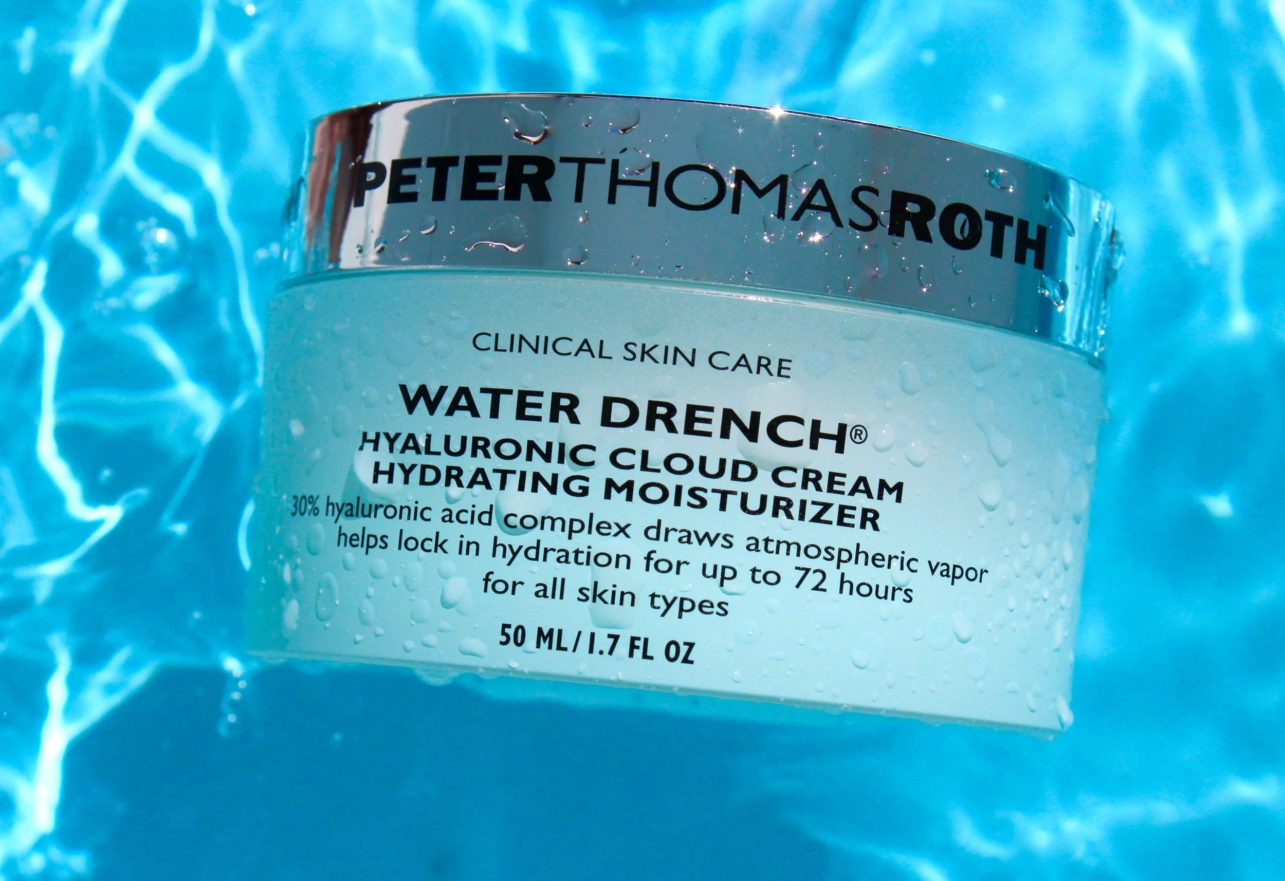 Close-up of a skincare product jar labeled 'Peter Thomas Roth Water Drench' with droplets of water on the surface, submerged in water with a rippling blue effect.