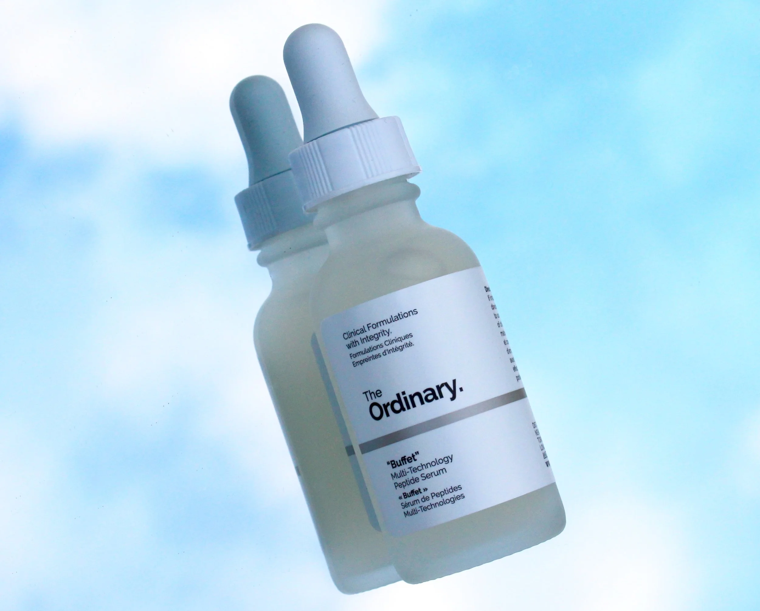 A white cosmetic bottle with a dropper cap against a light blue background.