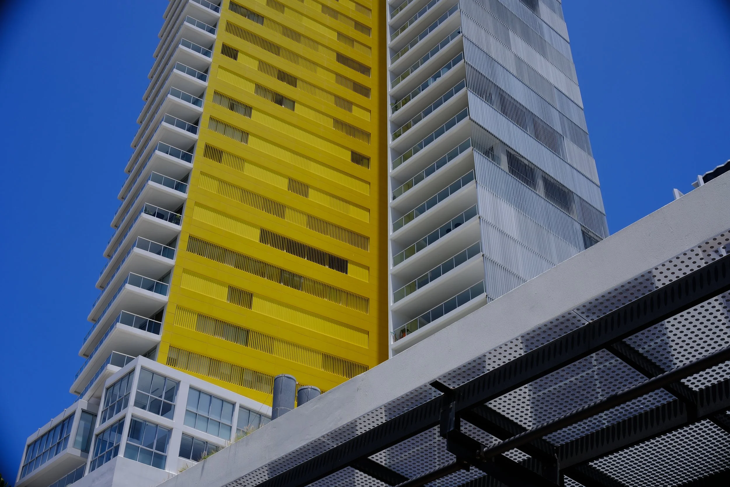 Modern high-rise building with yellow and white exterior, glass balconies, and a clear blue sky.