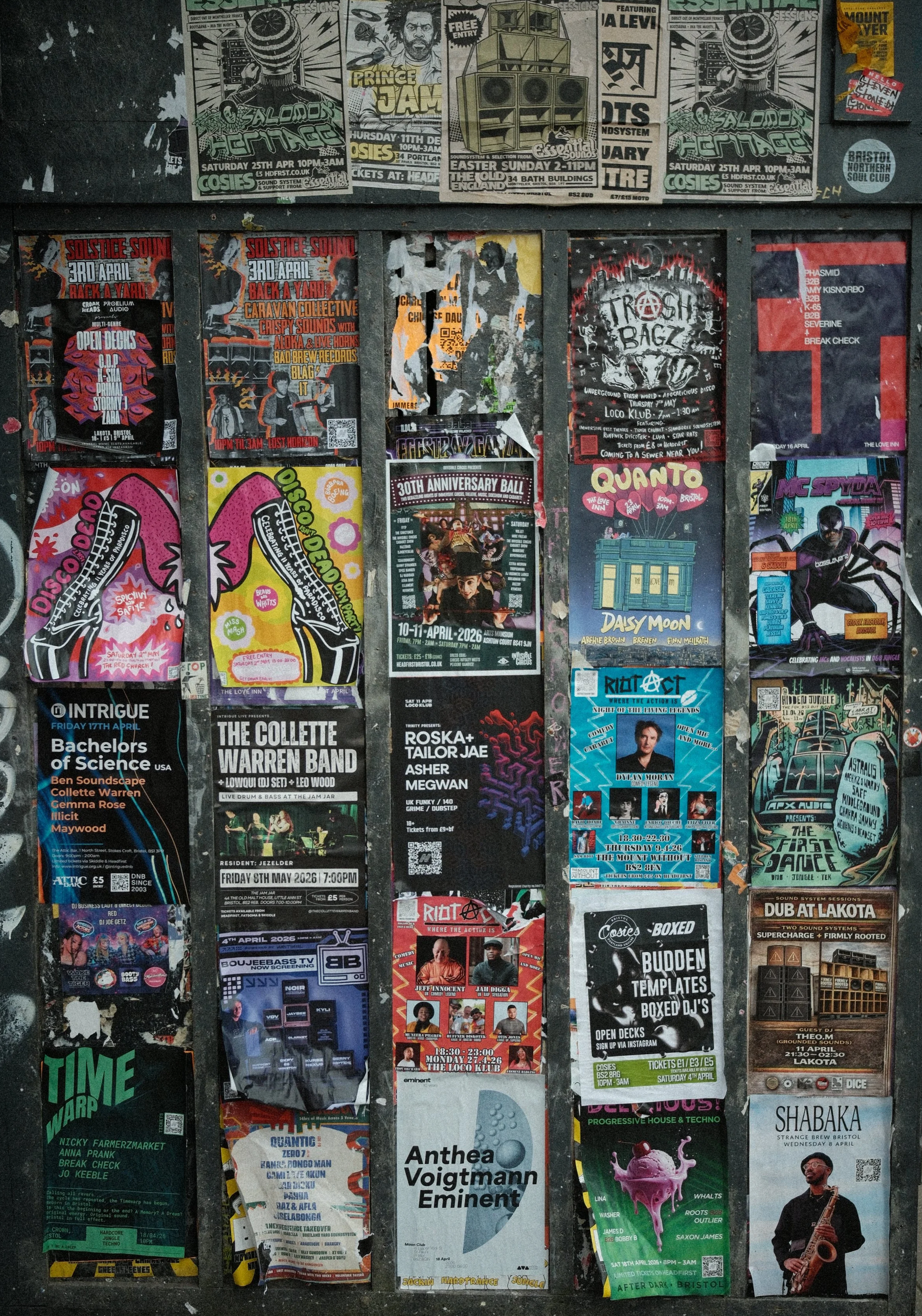 A wall covered with various colorful event flyers, posters, and advertisements for music nights, concerts, and parties, including genres like techno, house, and jazz, with some featuring artwork of DJs and performers.