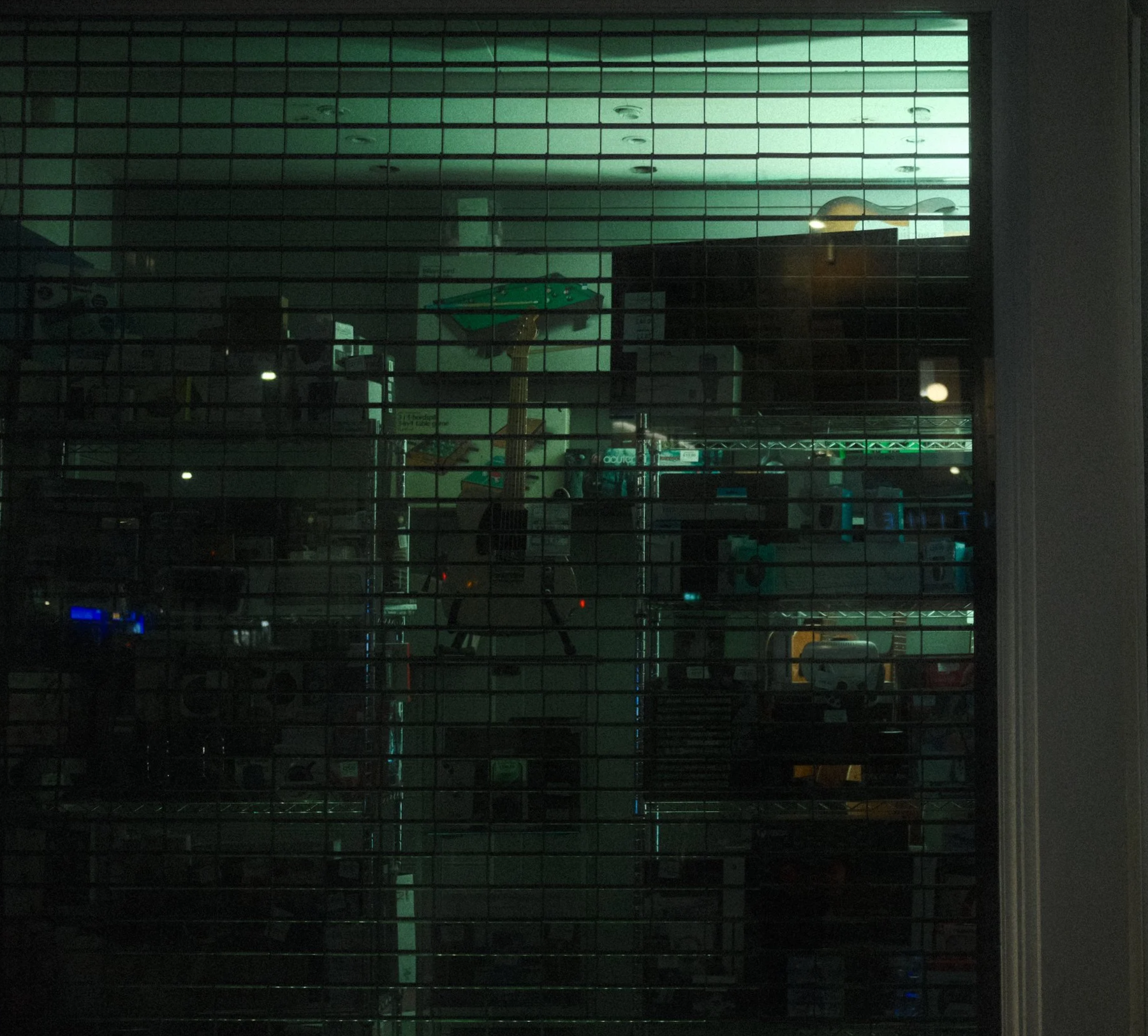 View through a closed glass window with horizontal blinds showing an indoor space with arcade games and a golf simulator.