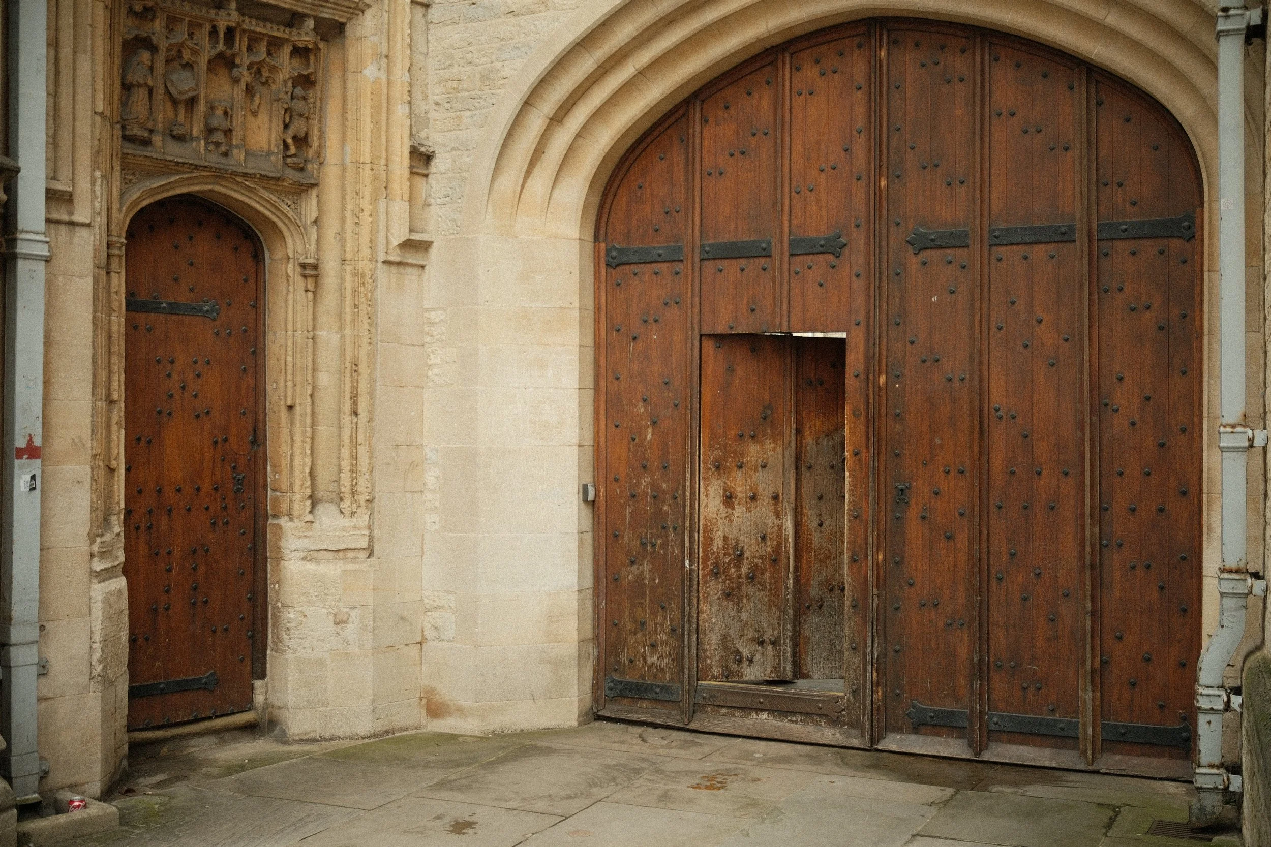 Large decorative wooden church or cathedral door with black metal studs and hinges, flanked by stone and brick architecture.