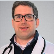 A man wearing glasses and a white lab coat, smiling against a plain background.