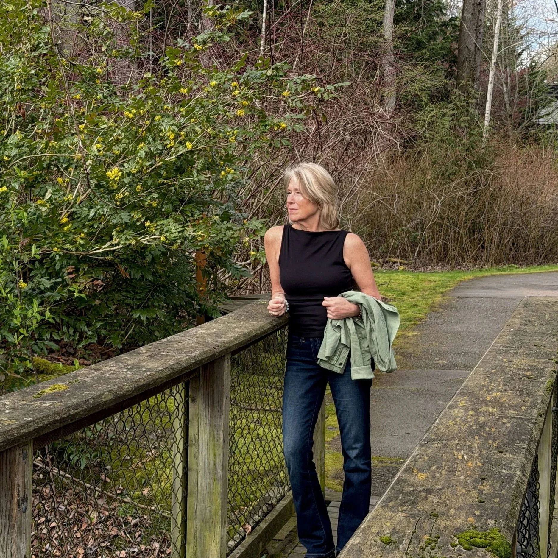 Seattle life coach Paula Freeman of Affirmative Coaching is standing near a wooden railing in a park on an overcast day.
