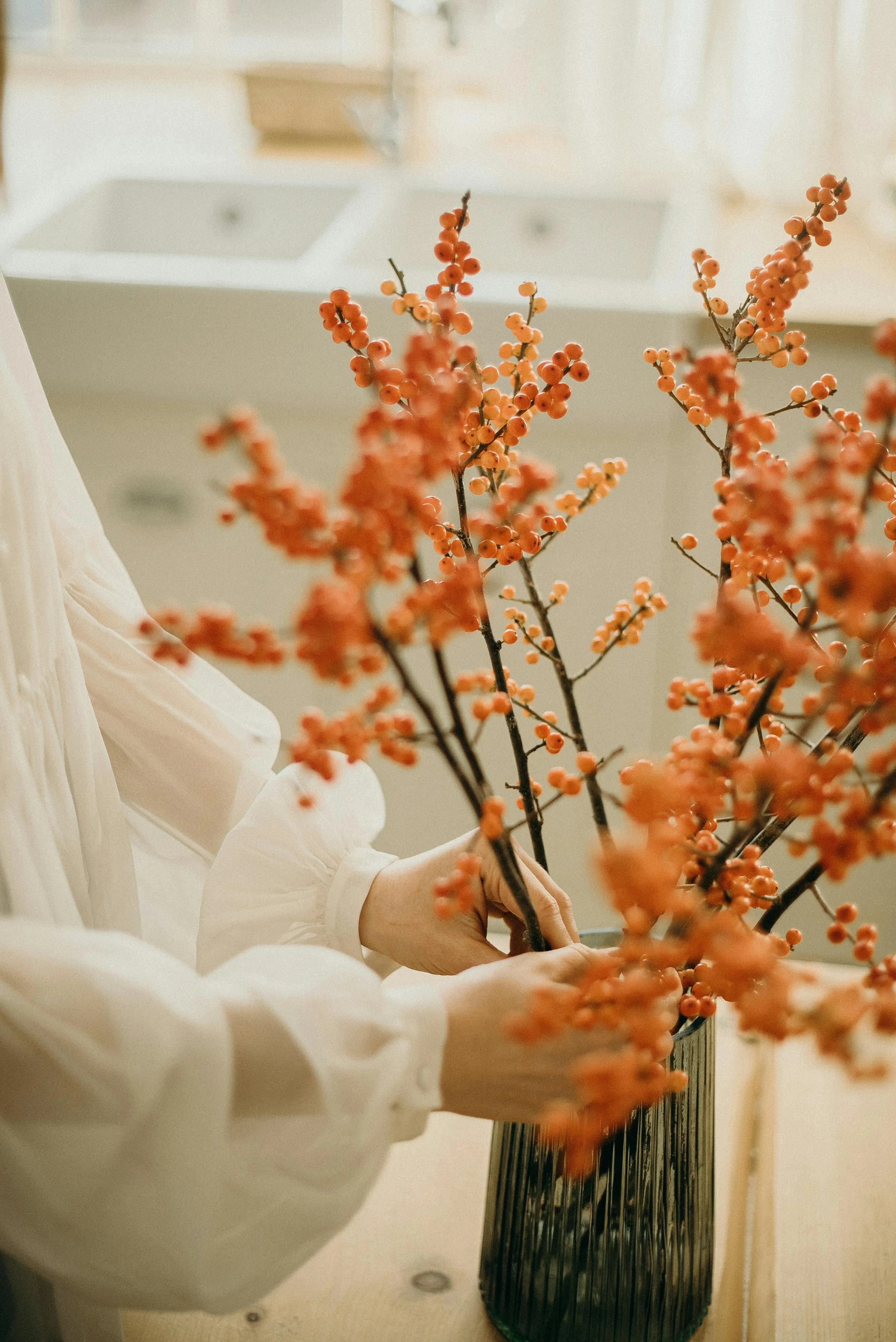 Person arranging orange berries on branches in a vase.