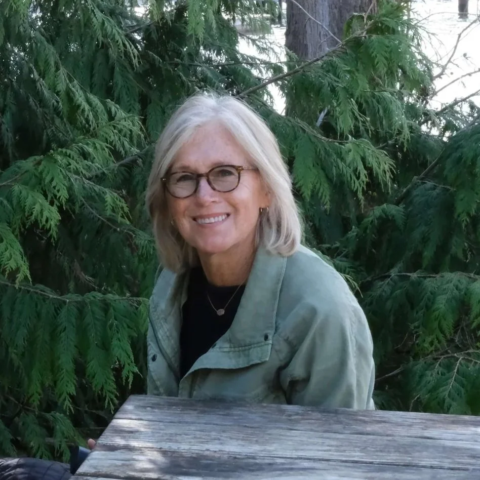 Seattle life coach Paula Freeman of Affirmative Coaching sits outdoors, surrounded by trees.