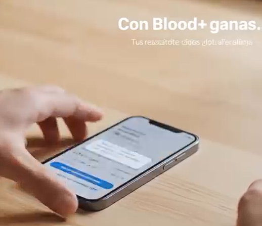 Una mano sostiene un teléfono inteligente en una mesa de madera, mostrando una pantalla con un chat. En la parte superior de la imagen hay texto en español que dice 'Con Blood+ ganas', y debajo en letra más pequeña 'Tus resultados así lo dicen.'