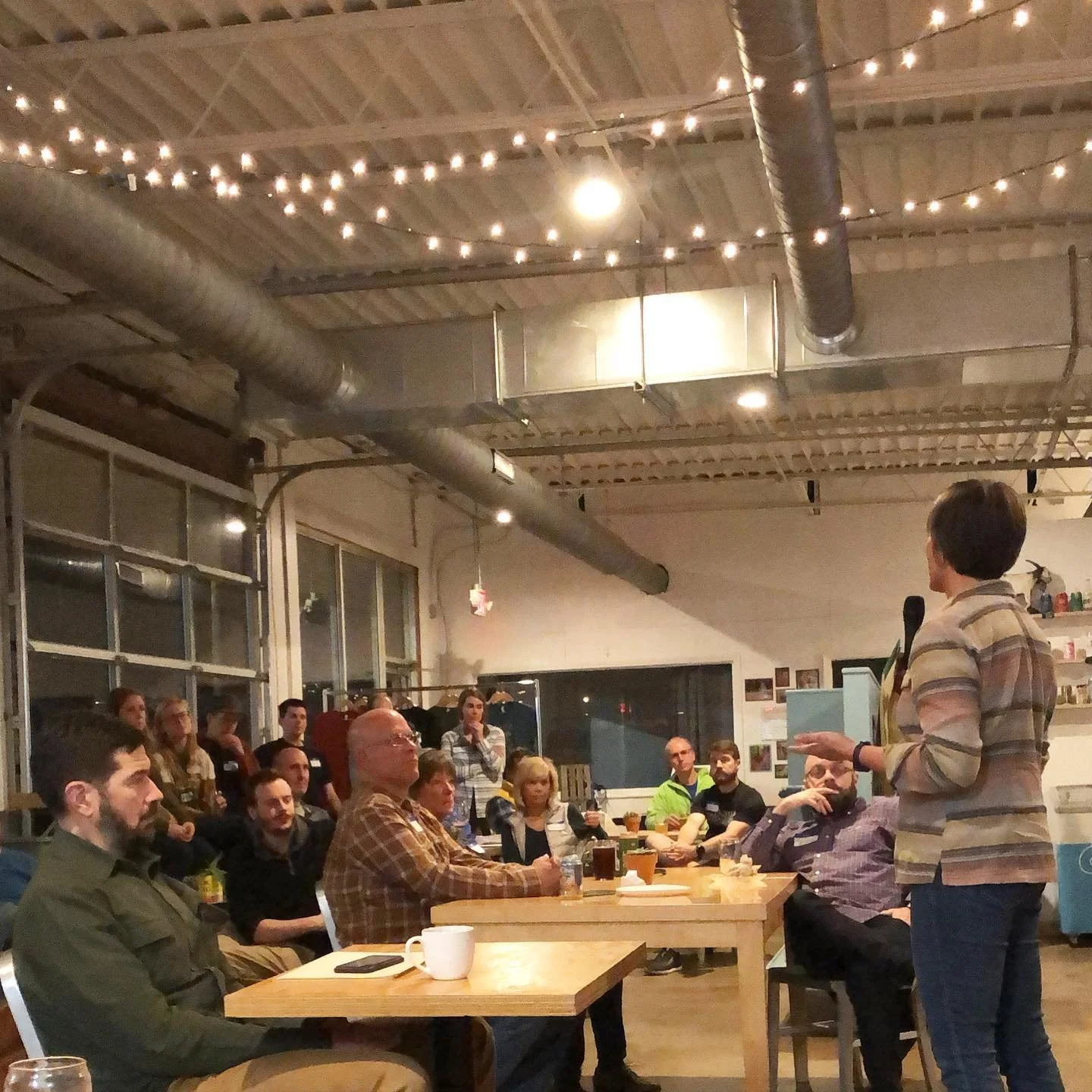 Naomi, the General Manager of Greenville's REI location, is speaking into a microphone at an Upstate Stewards meeting at Mountain Goat coffee shop.