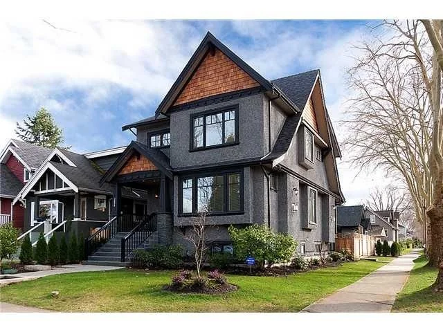 Modern gray and wood-paneled two-story house with front porch, black stairs, and landscaped yard in a suburban neighborhood.