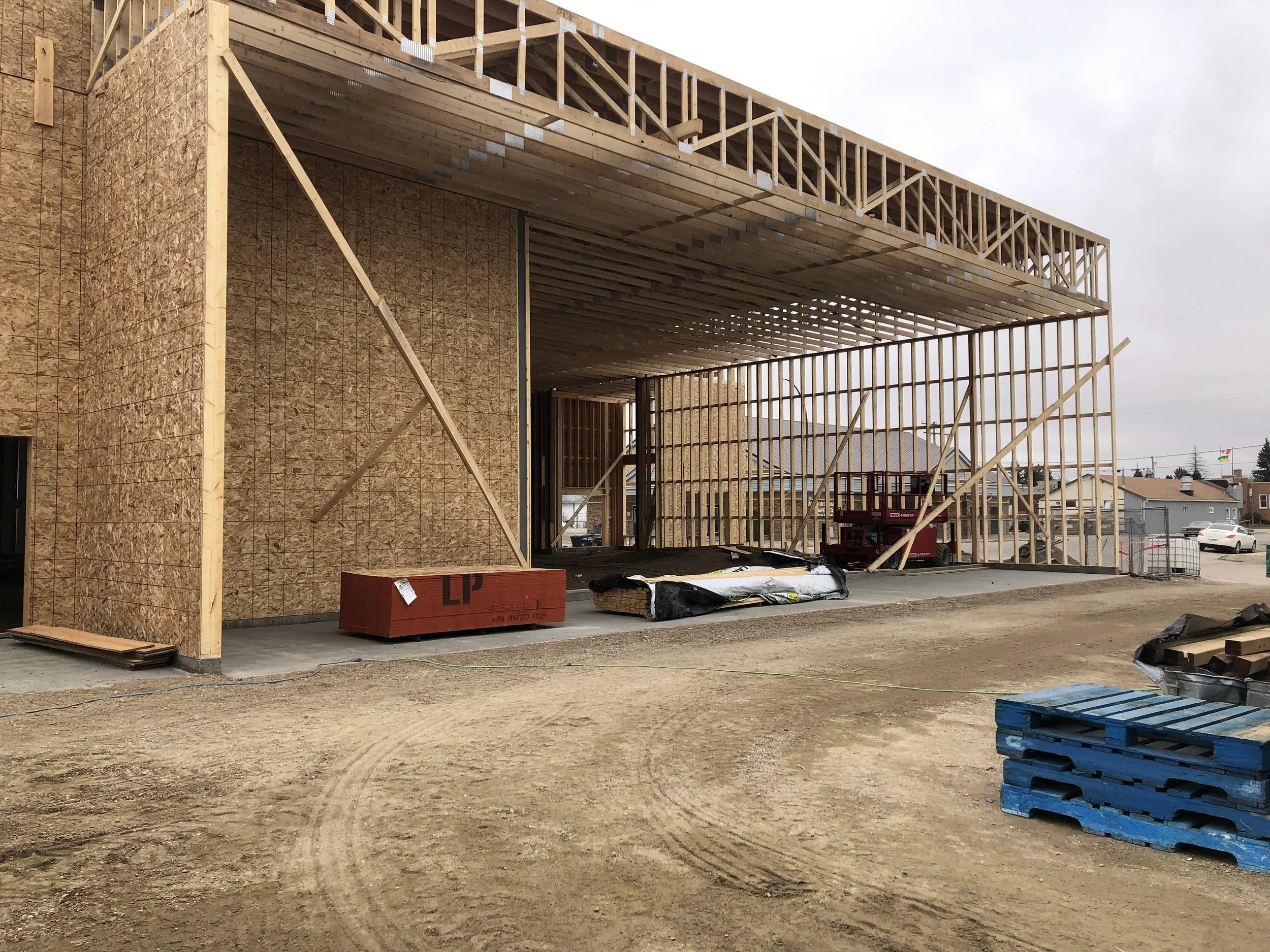 Construction site with wooden framing for a building, scaffolding, and construction materials on dirt ground.