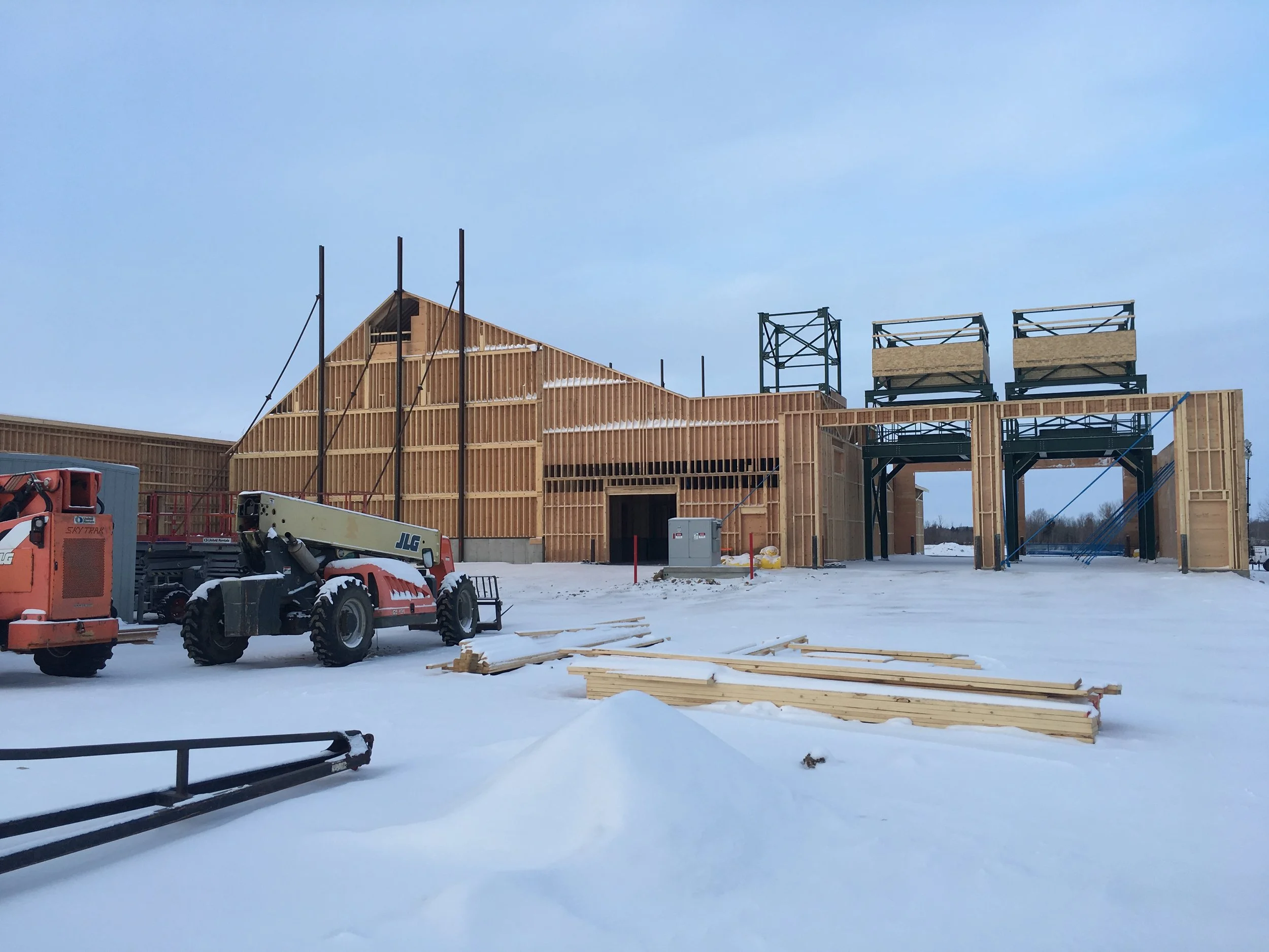 Construction site with wooden framing for a building, construction equipment including a cherry picker, and snow on the ground and structure during winter.