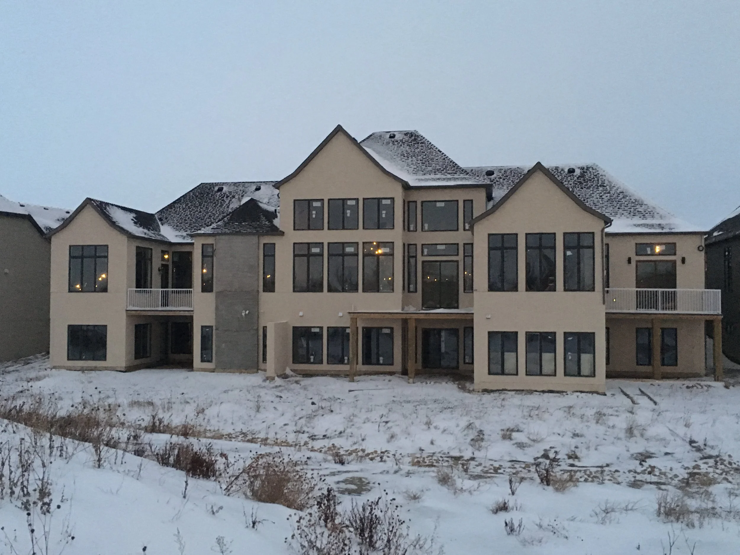A large multi-story house with multiple windows and snow on the roof, surrounded by snow-covered ground in a winter setting.