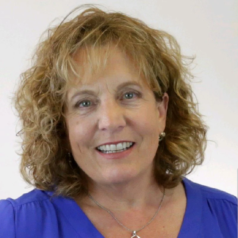 A woman with curly blonde hair, wearing a blue top, smiling at the camera.