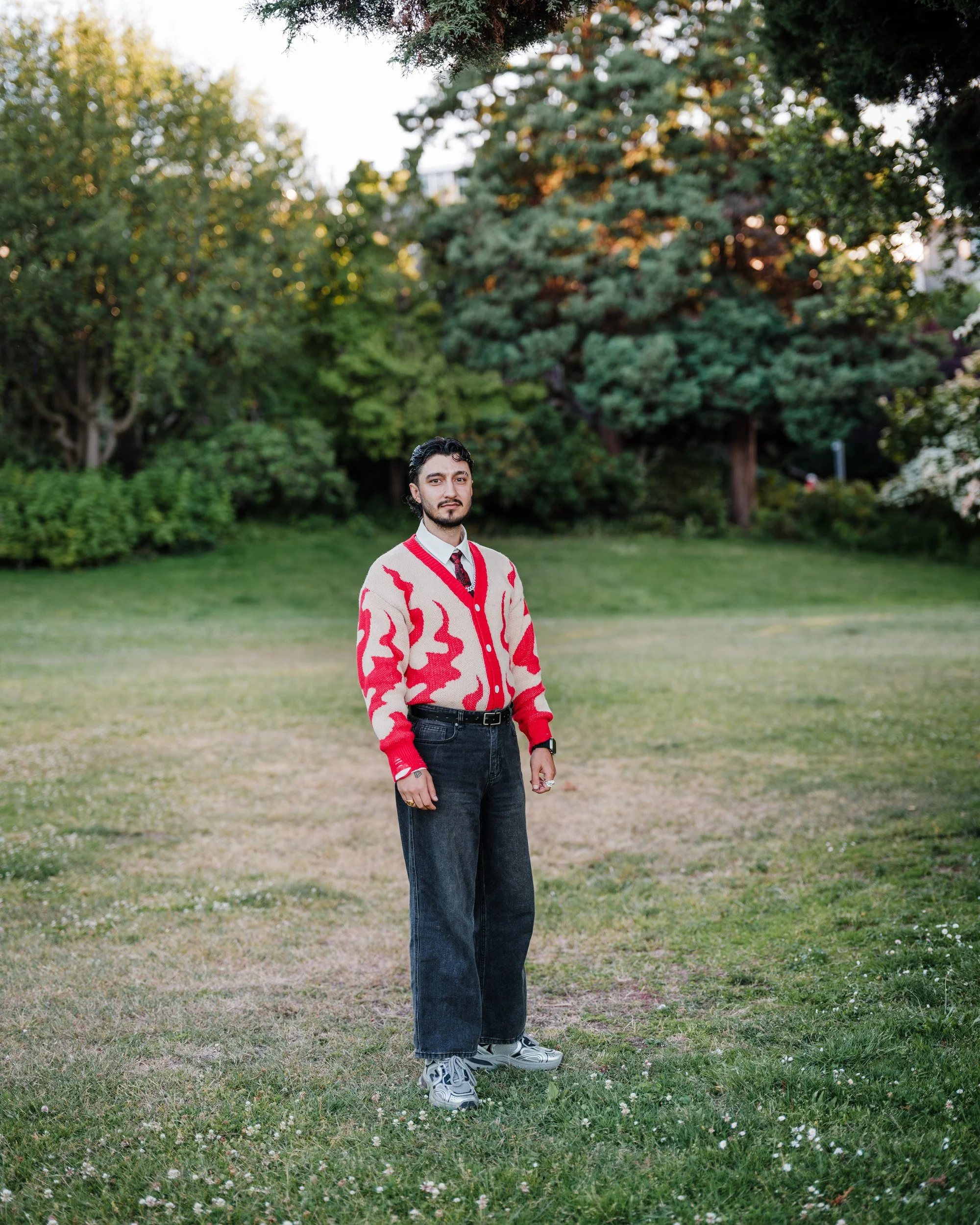 Young man in a red and white patterned sweater stands in the middle of a grassy park