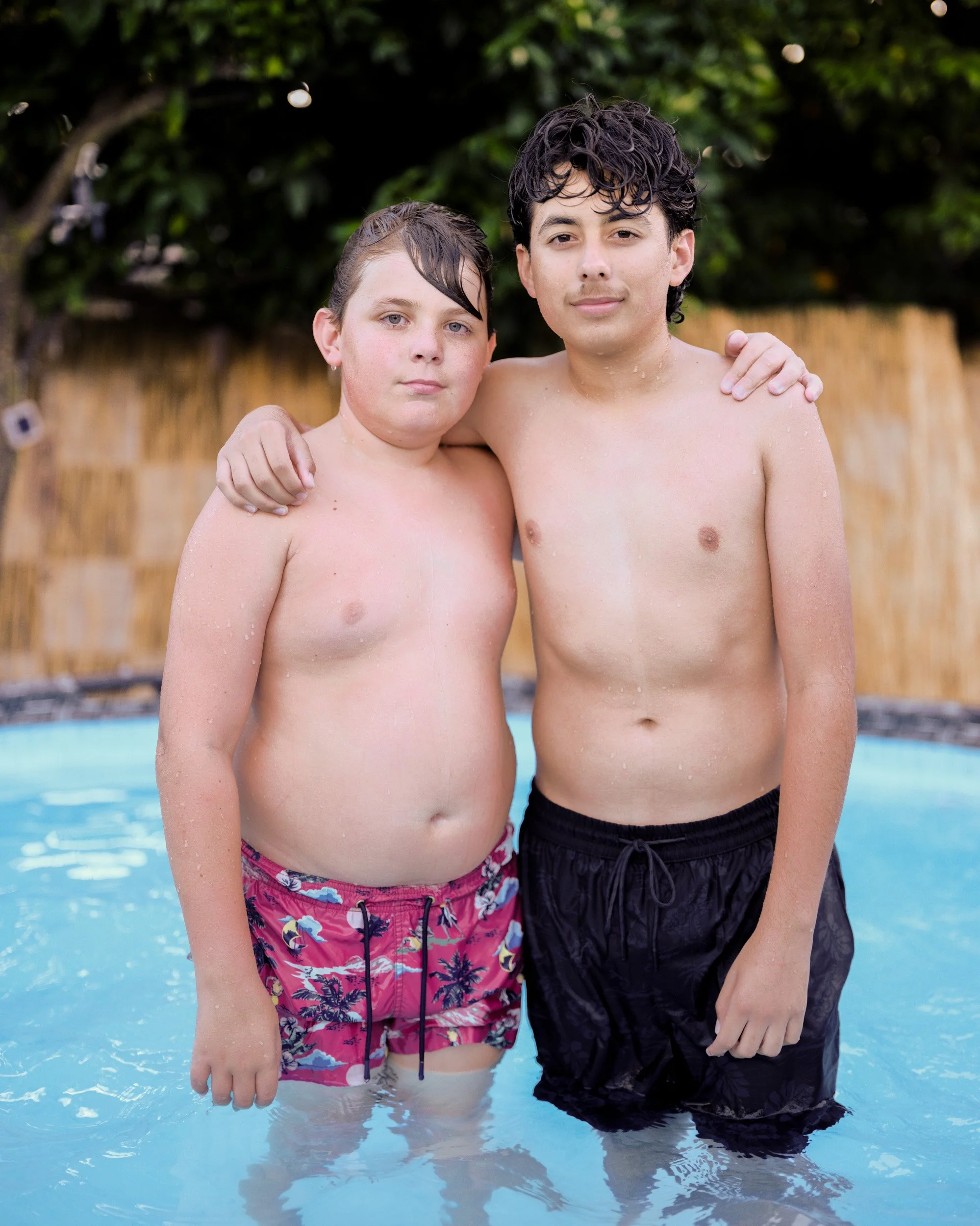 Two brothers stand arm in arm in a backyard swimming pool