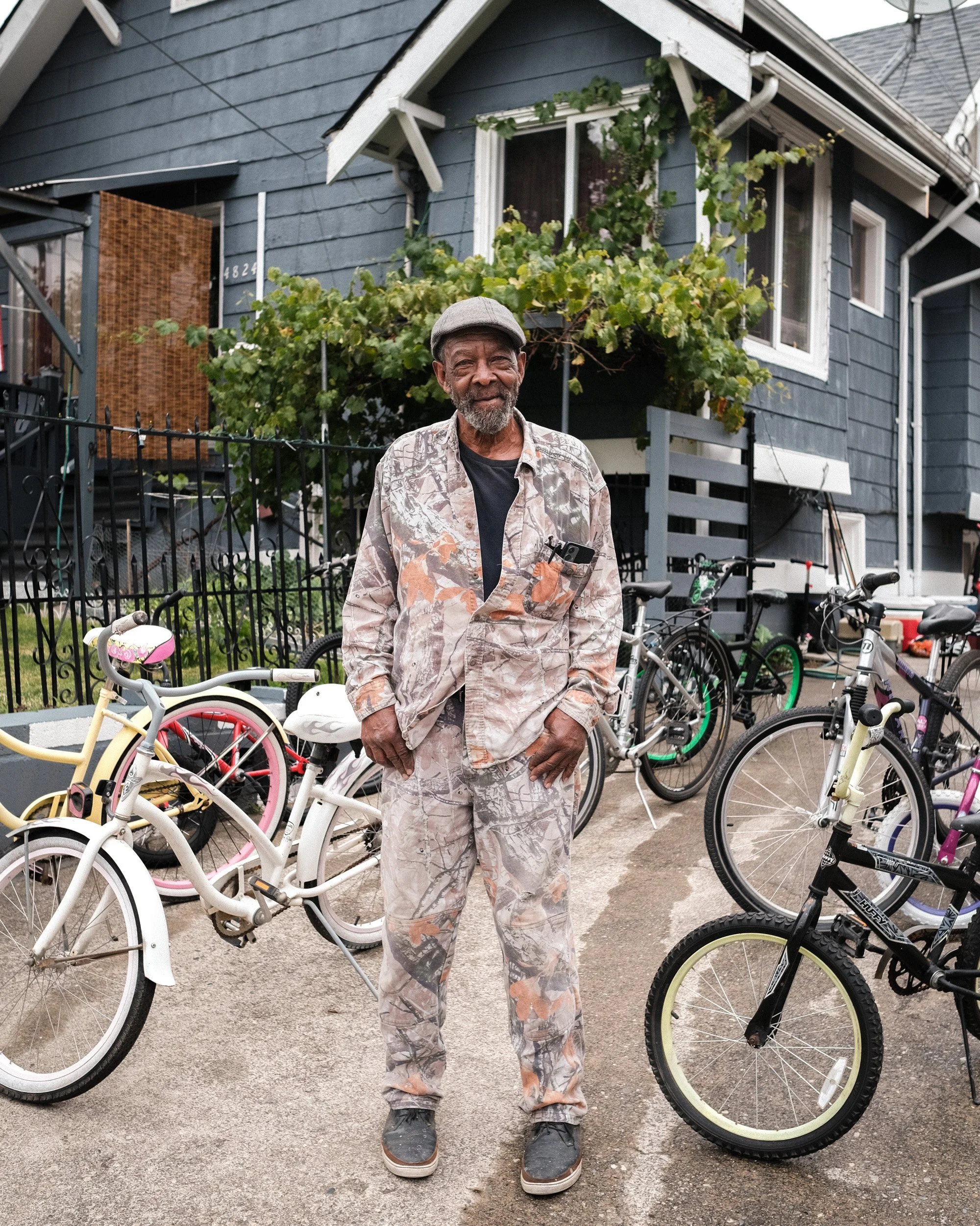 Man in a patterned jacket and matching pants stands among parked bicycles outside a craftsman house