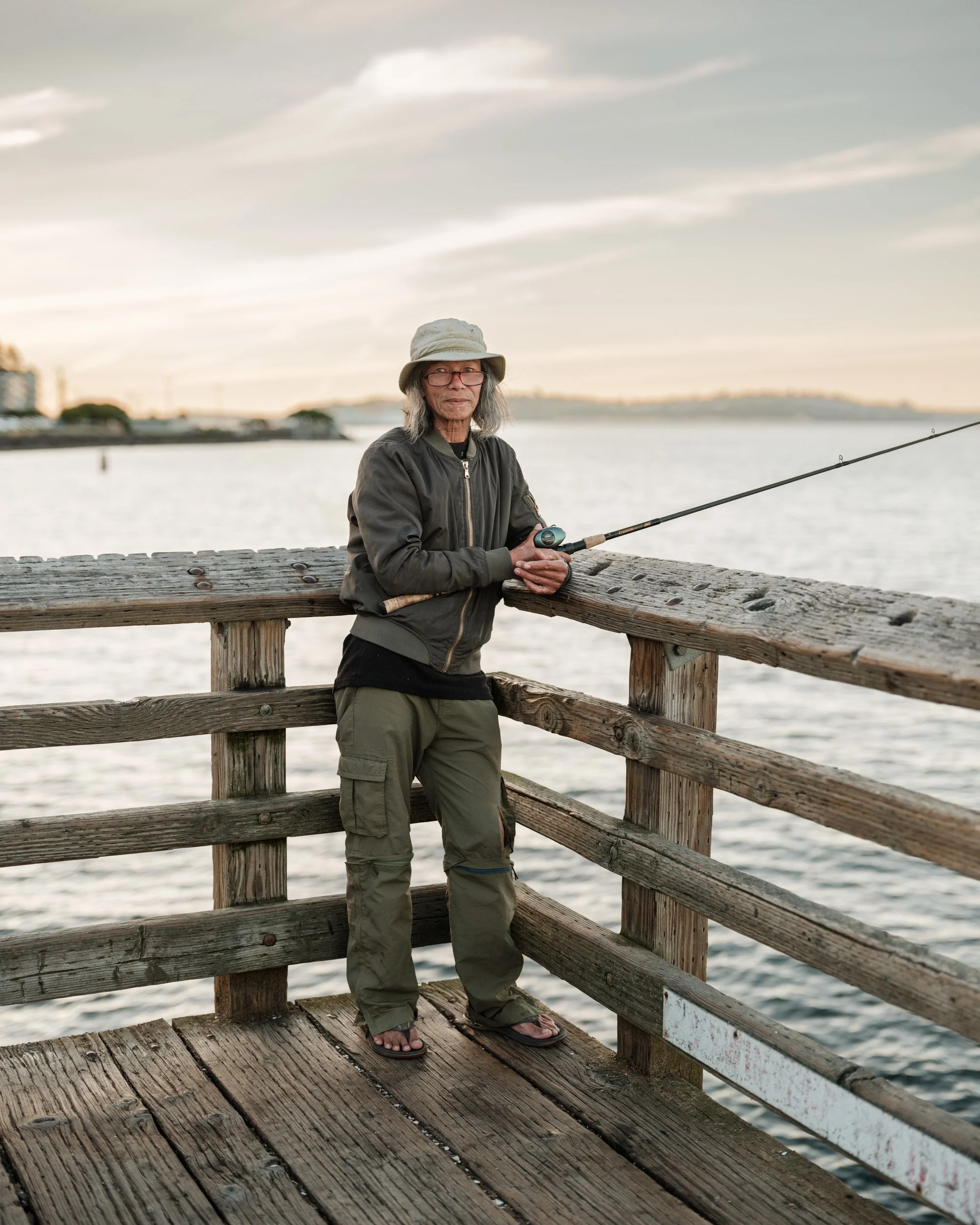 Man in a bucket hat fishes from a wooden pier on the Seattle waterfront
