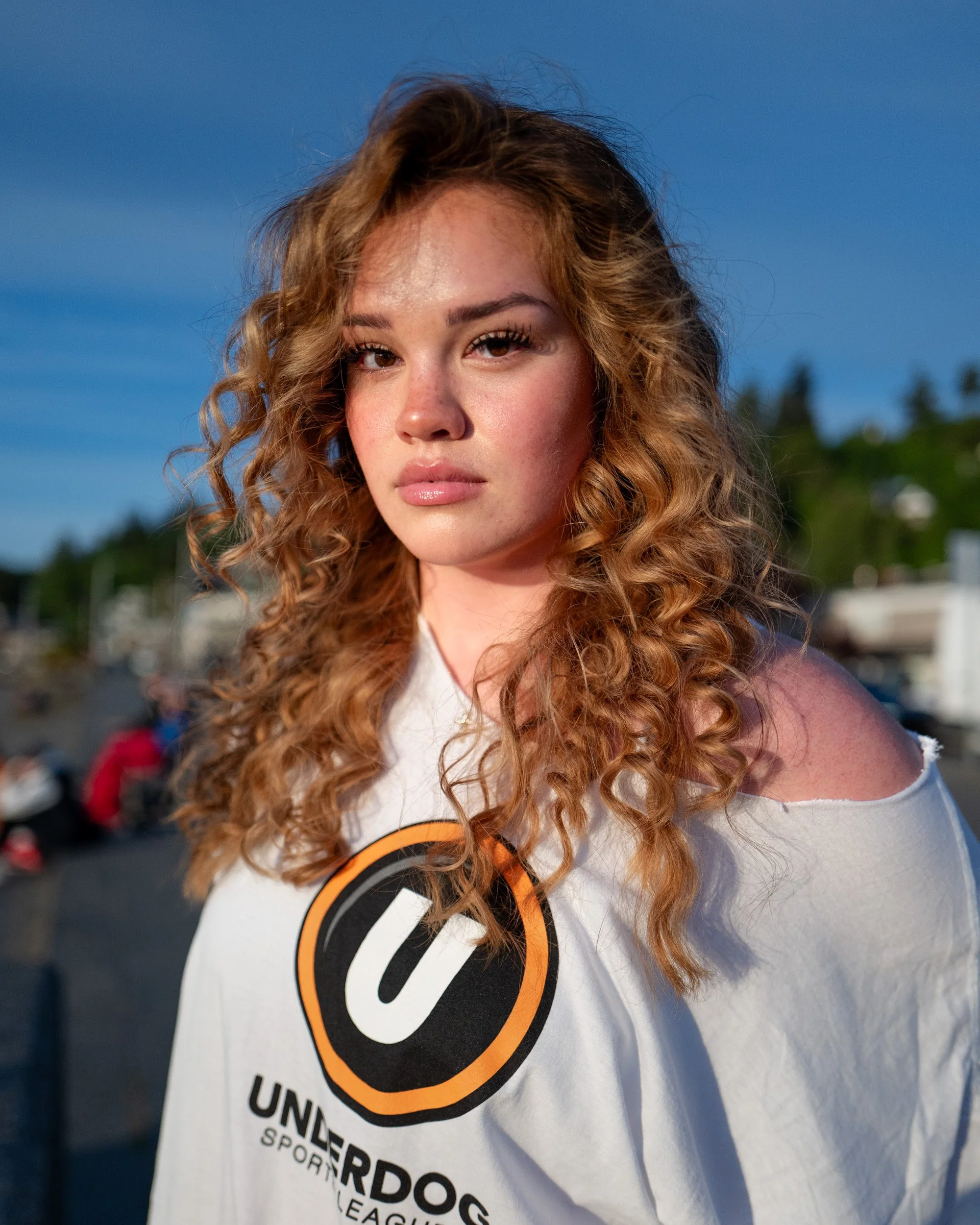 Portrait of a young woman with long curly hair in an off-the-shoulder sweatshirt at dusk
