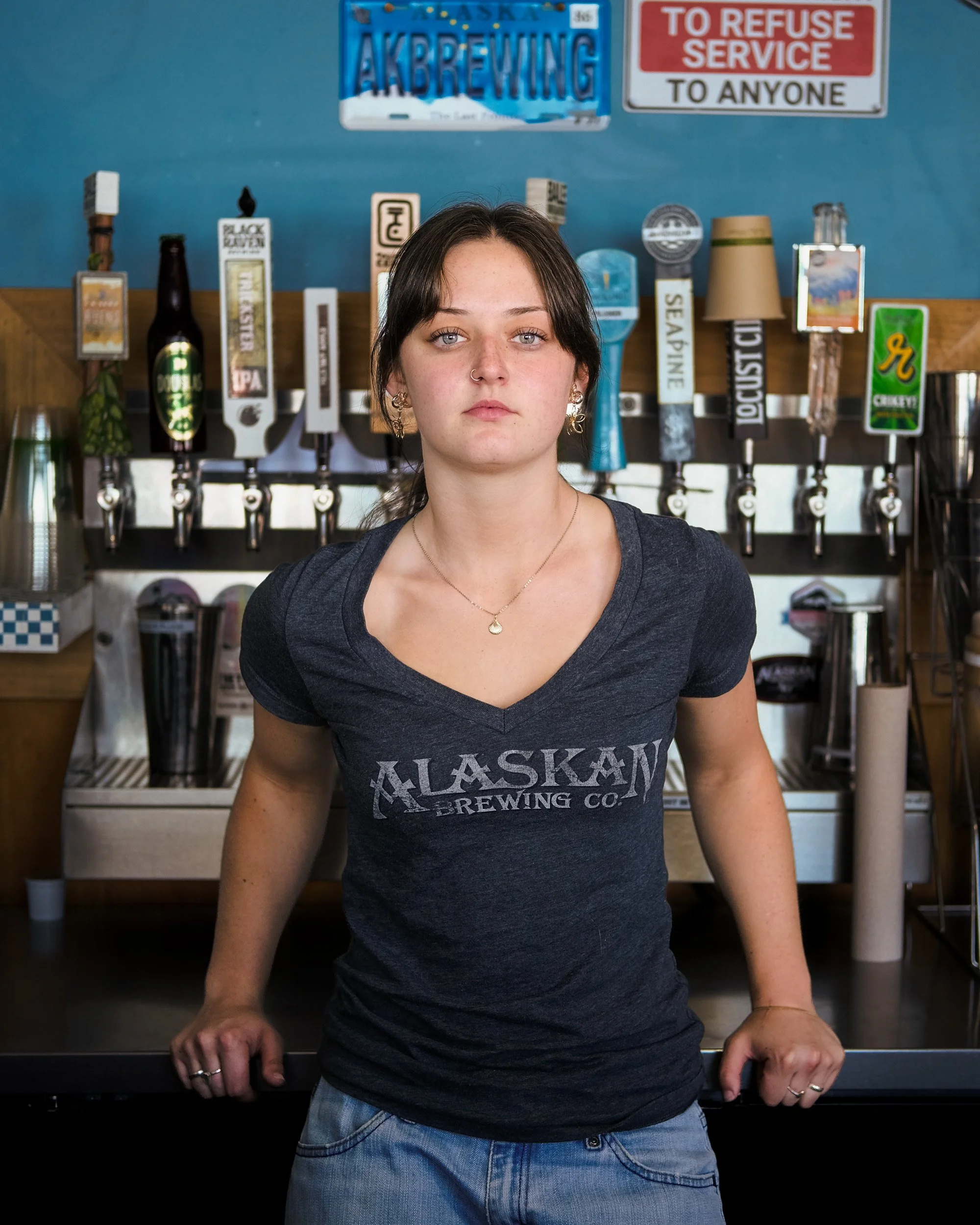 Young woman leans on a bar counter in front of a row of beer taps