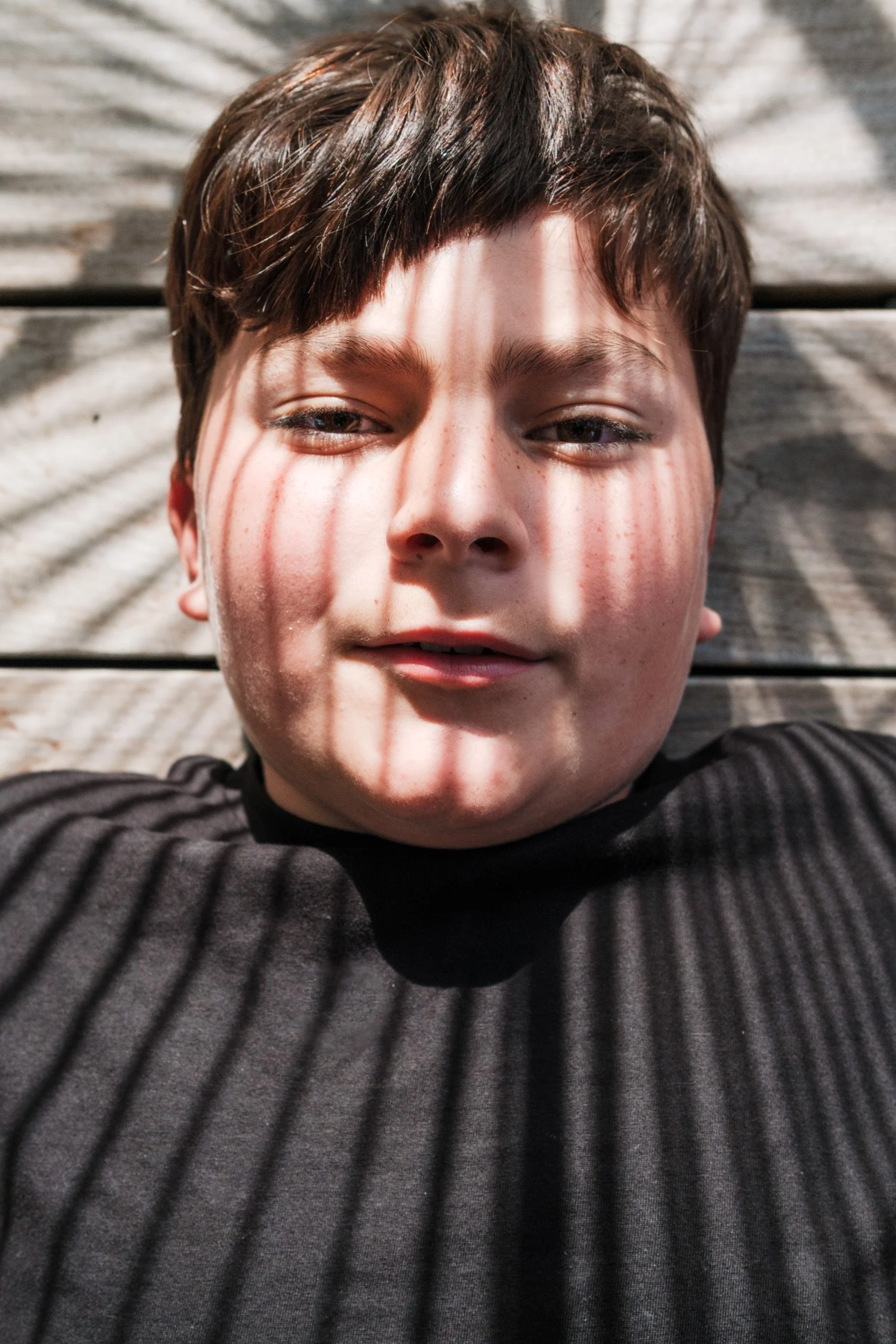 Close-up of a boy's face striped with shadows from window blinds