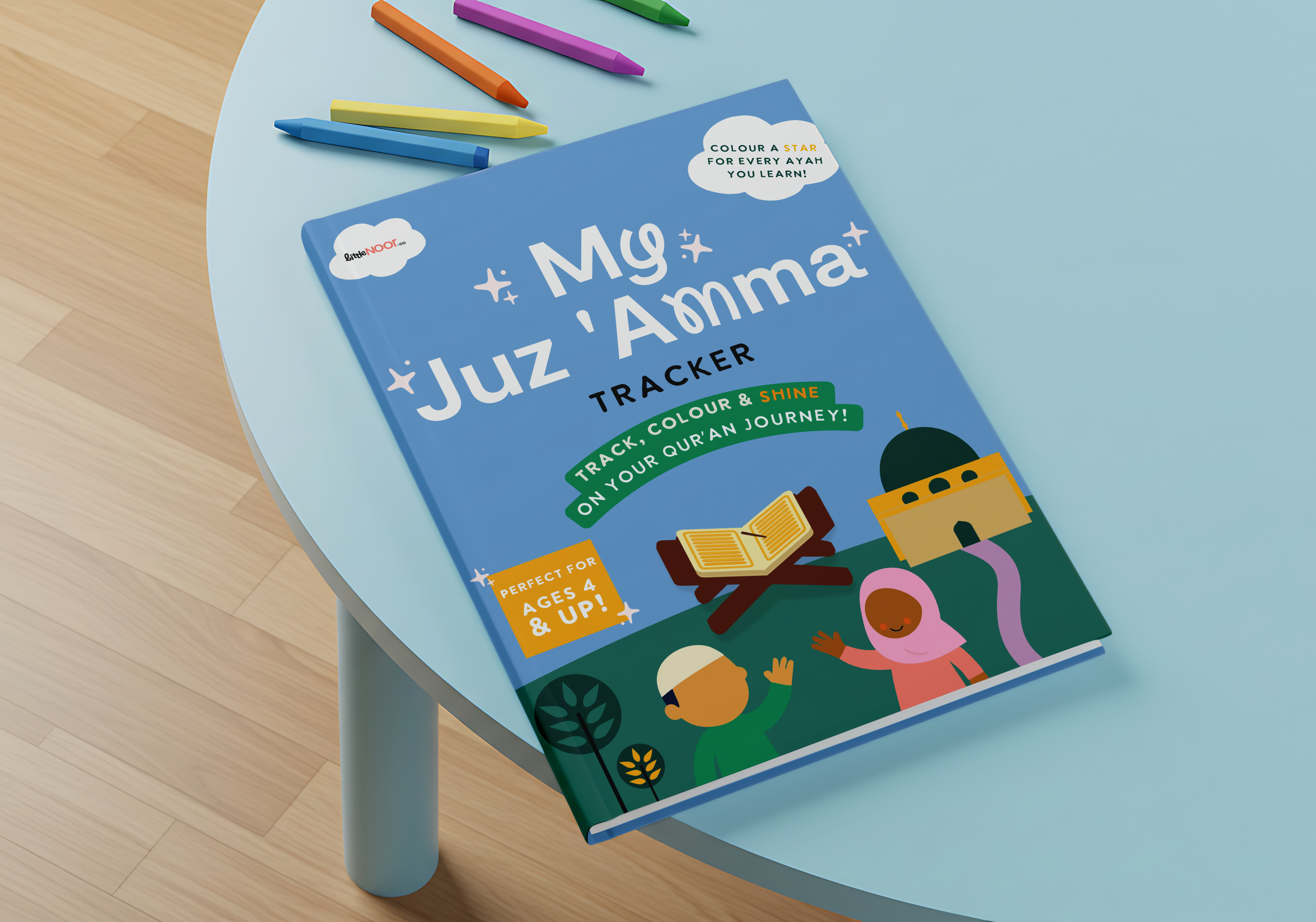 A children's book titled 'My Juz' Amma' on a light blue table, with colorful markers nearby, featuring illustrations of children and a mosque.