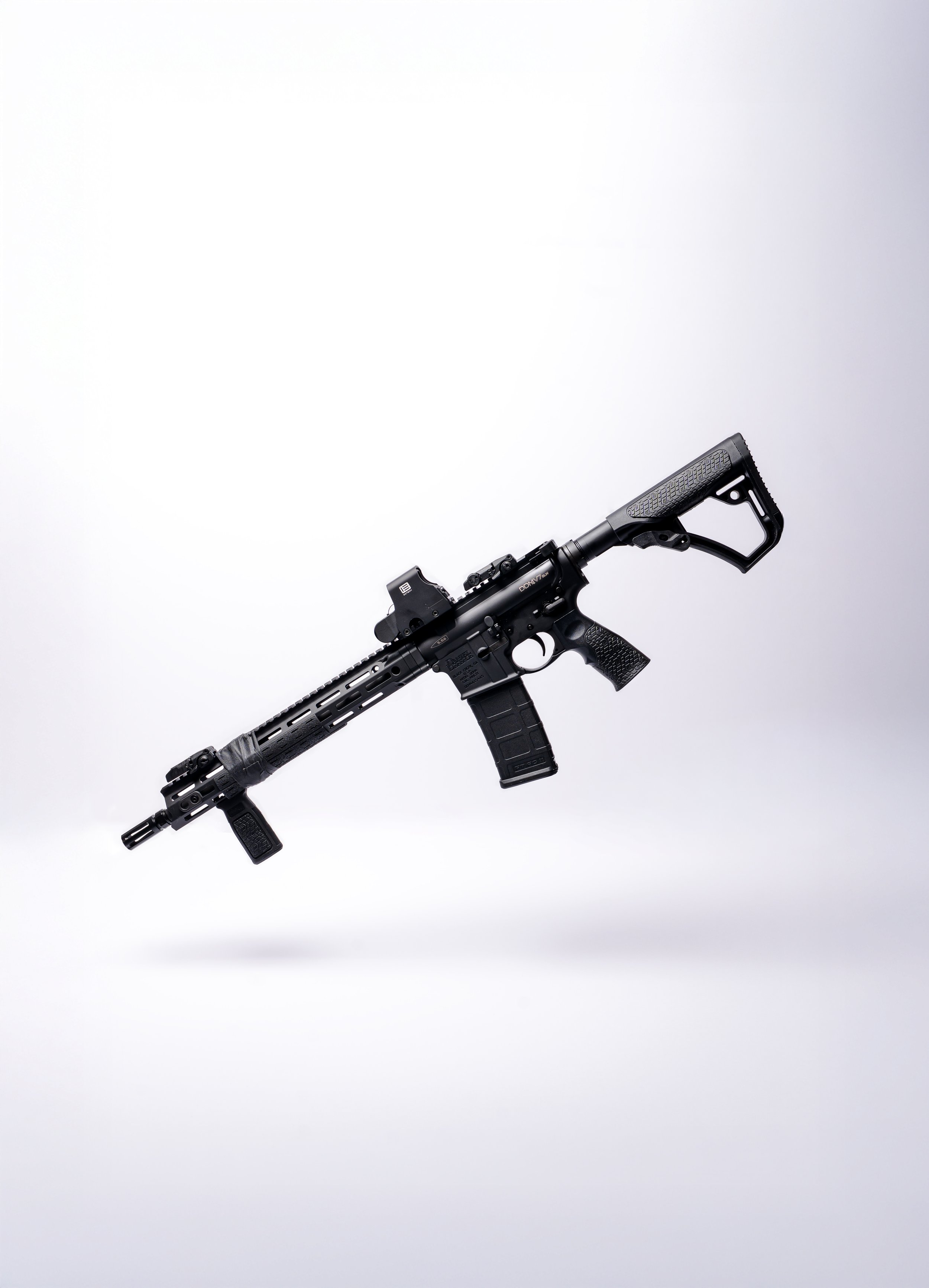 A black rifle with a mounted scope, adjustable stock, tactical grip, and a rail system, positioned diagonally against a plain white background.