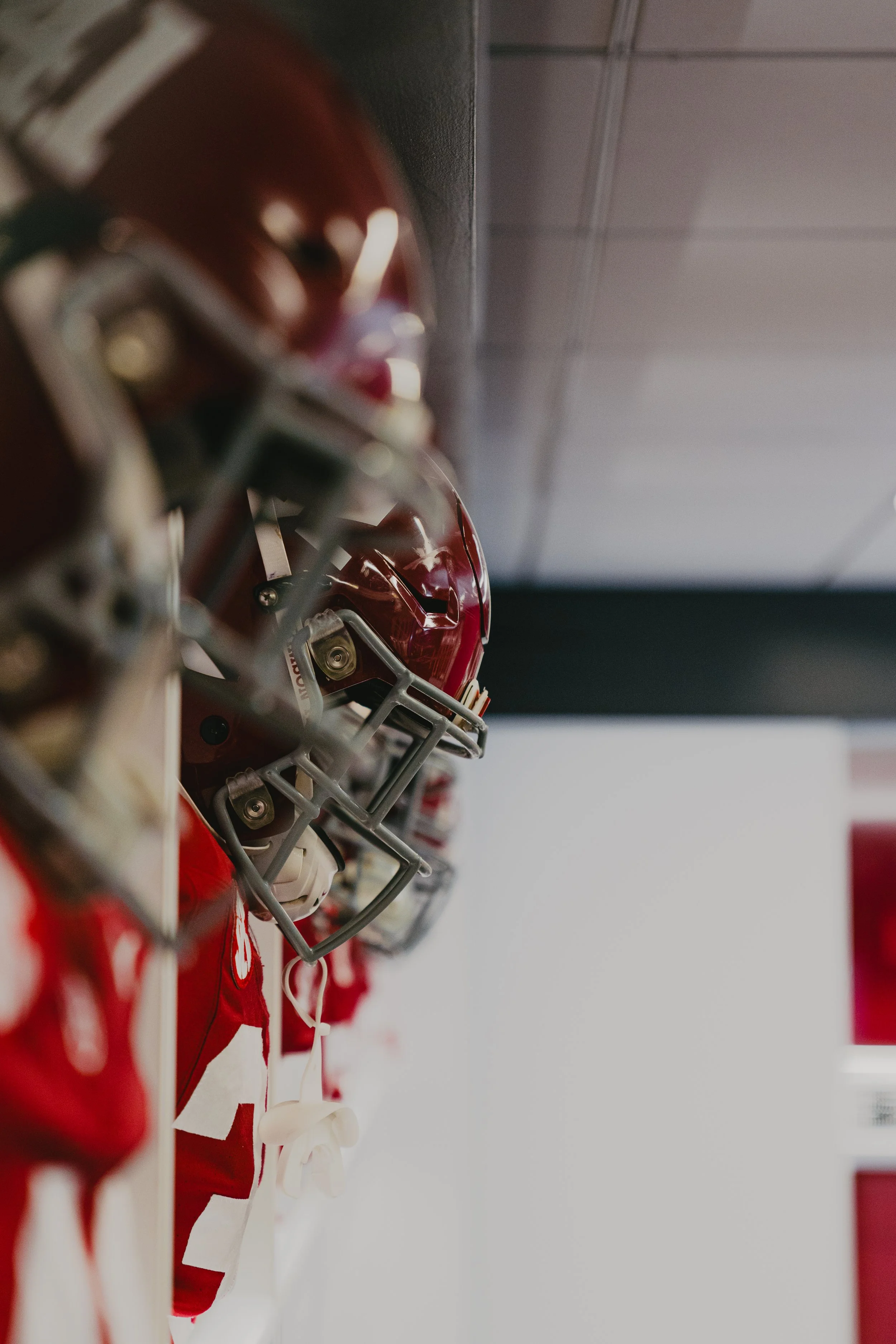 Close-up of red sports helmets and jerseys hanging on a wall in a locker room.