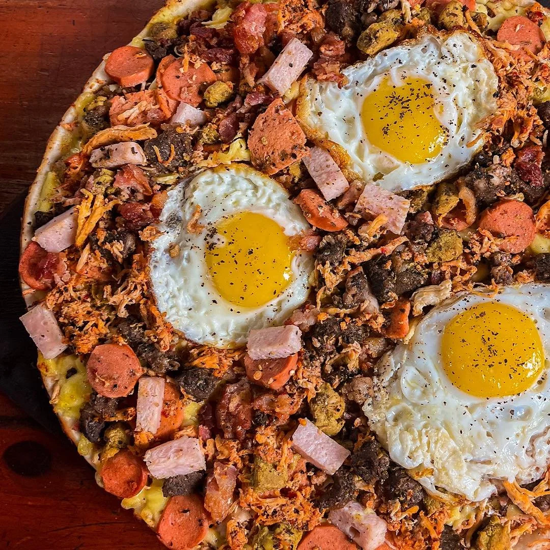 Pizza topped with fried eggs, sliced sausage, diced ham, ground meat, and vegetables.