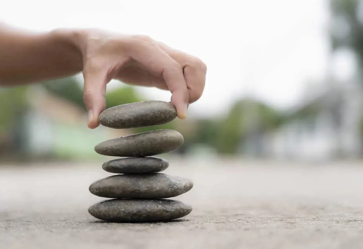 Una mano colocando piedras en equilibrio una encima de otra en un ambiente exterior.