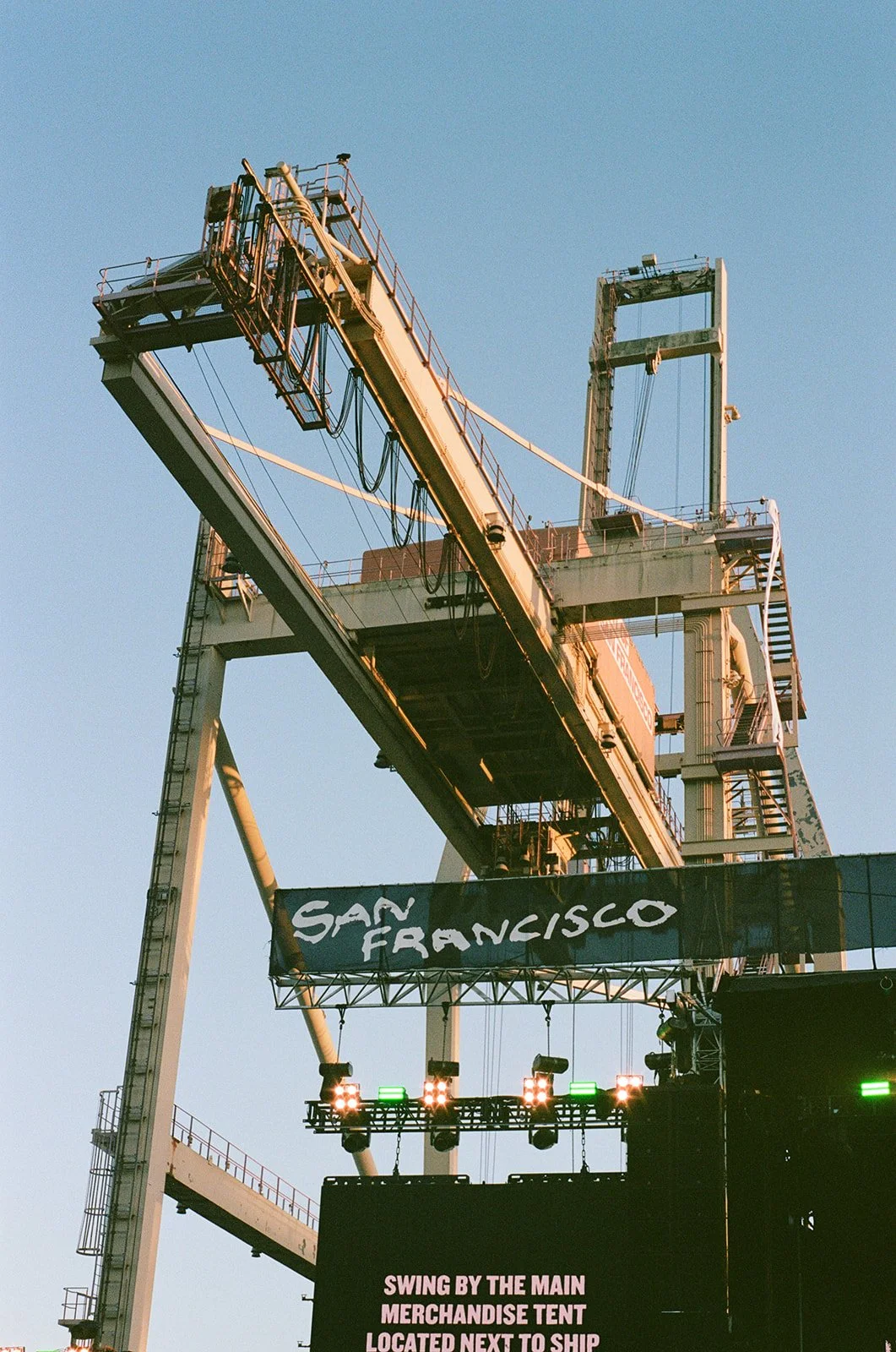 A large industrial crane with a banner that reads 'San Francisco' and a smaller screen with event information, set against a clear blue sky.